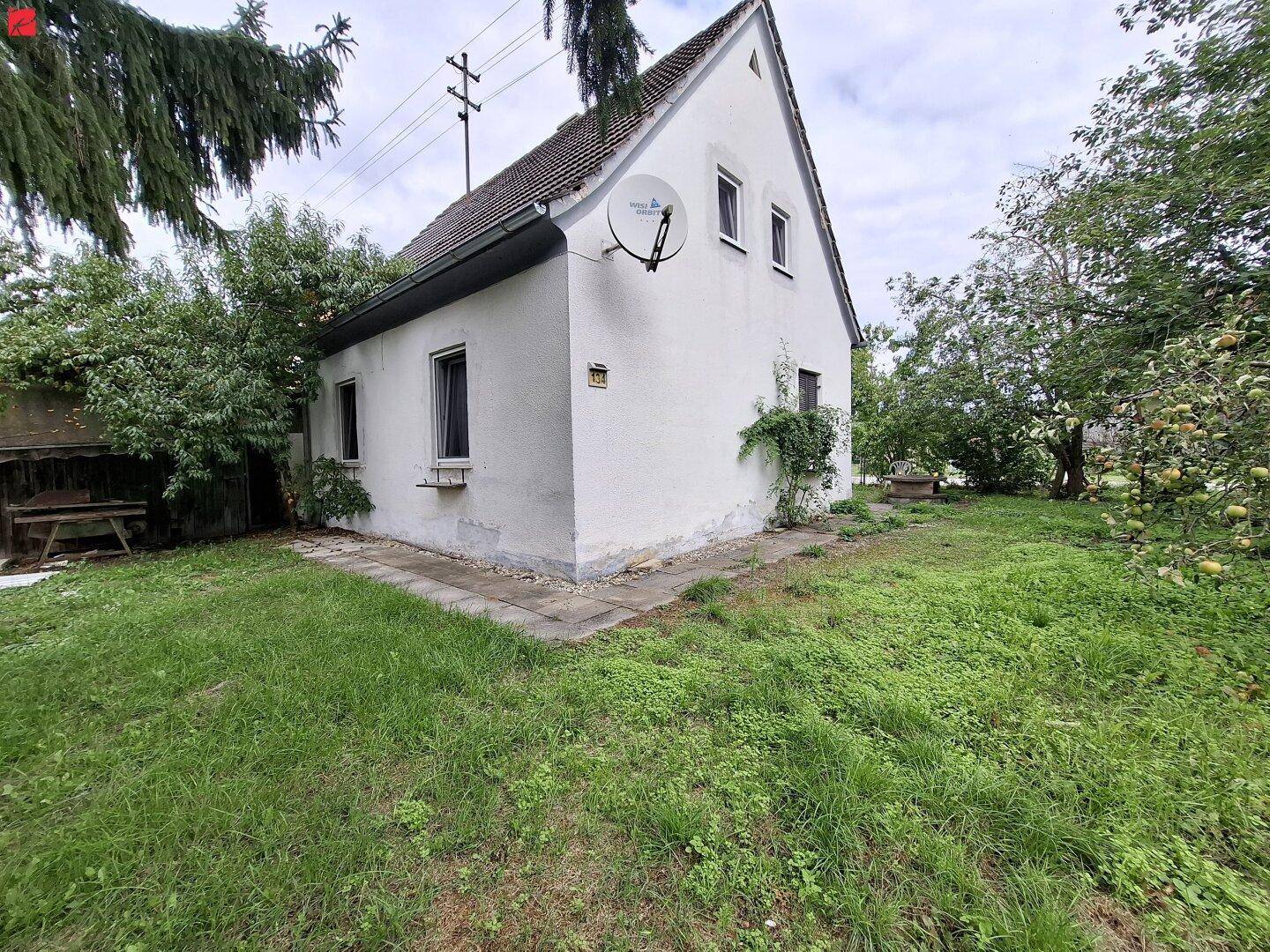 Freistehendes Haus mit Satteldach, umgeben von einem großen Garten mit Bäumen und Rasenfläche.