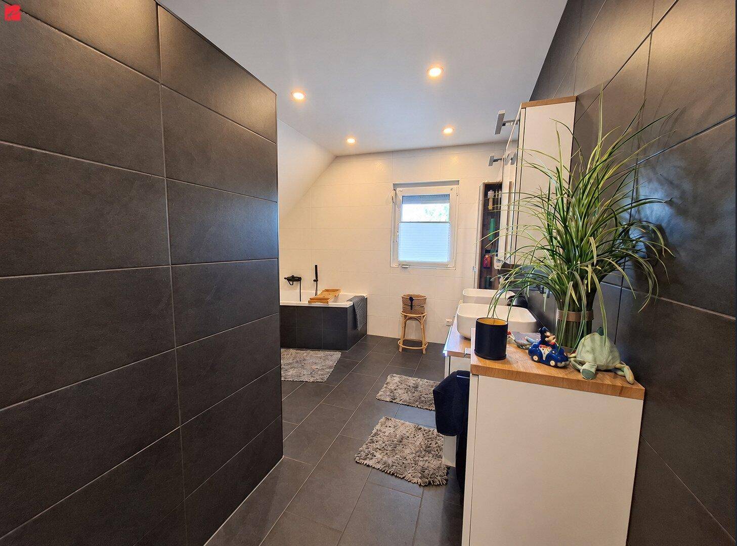 Modernes Badezimmer mit dunklen Fliesen, freistehender Badewanne und Fenster.