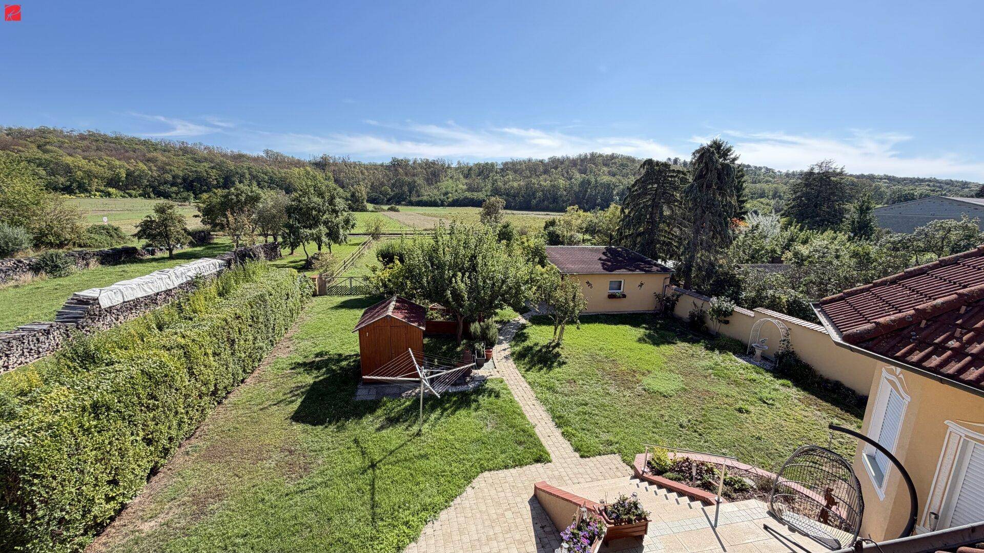 Weitläufiger Gartenbereich mit Rasen, Bäumen und Blick auf die umliegende Landschaft.