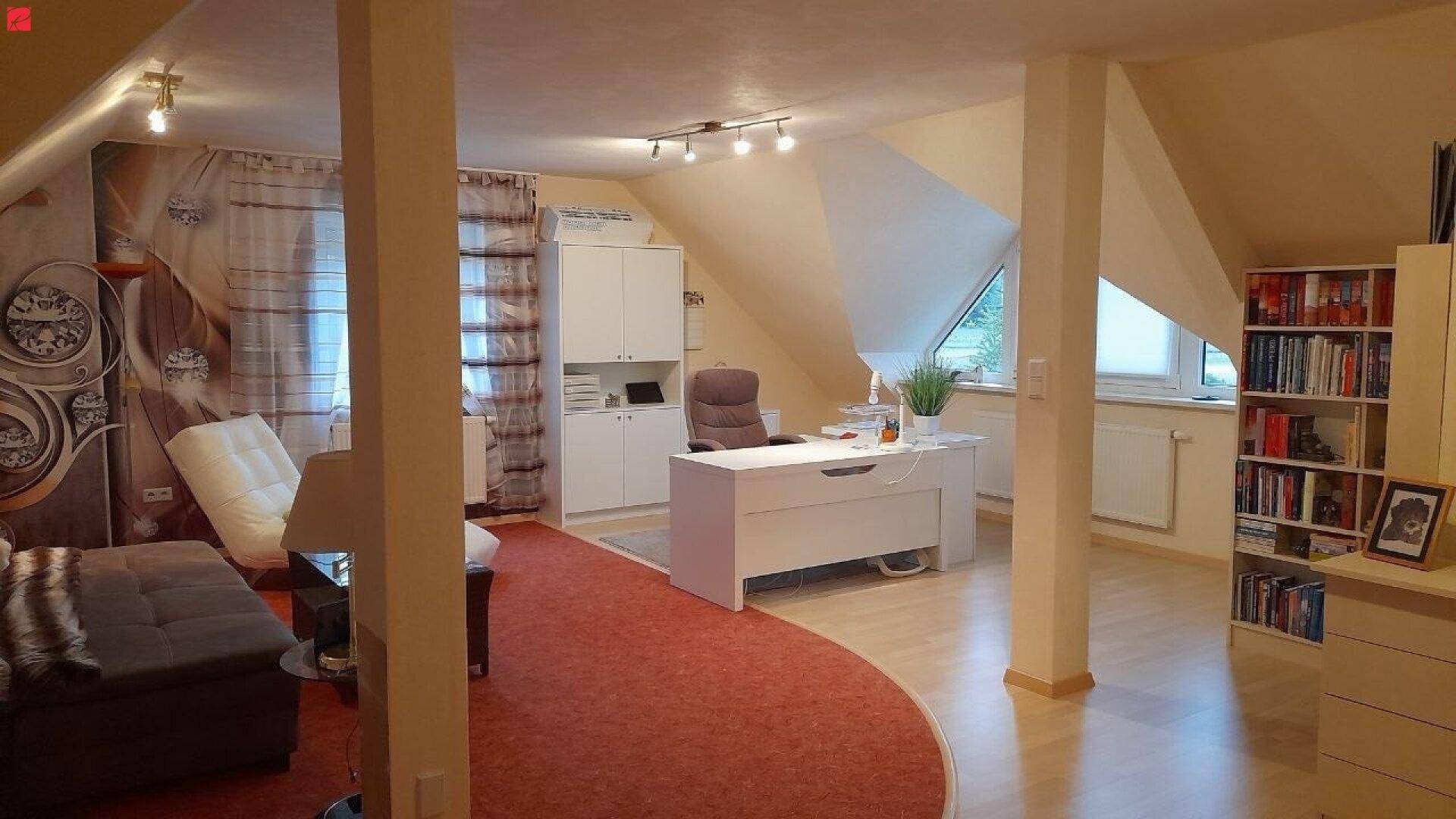 Helles Dachgeschosszimmer mit Arbeitsbereich, gemütlicher Sitzecke und schrägen Wänden.