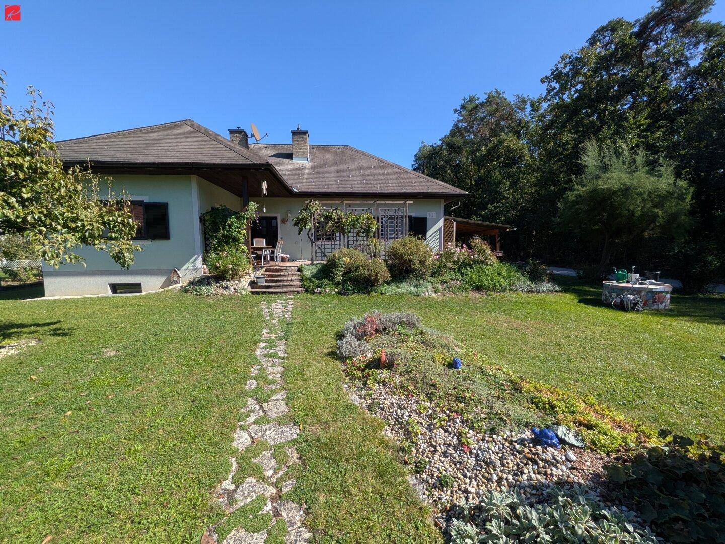 Rückansicht des Hauses mit gepflegtem Garten, Rasen und einer kleinen Terrasse mit Treppe.