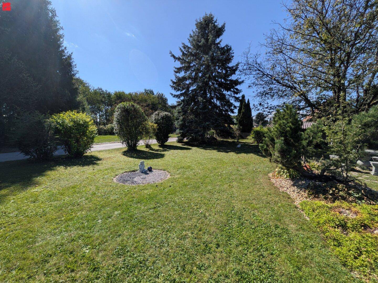 Weitläufiger Garten mit Rasenflächen, Bäumen und Sträuchern unter einem klaren blauen Himmel.