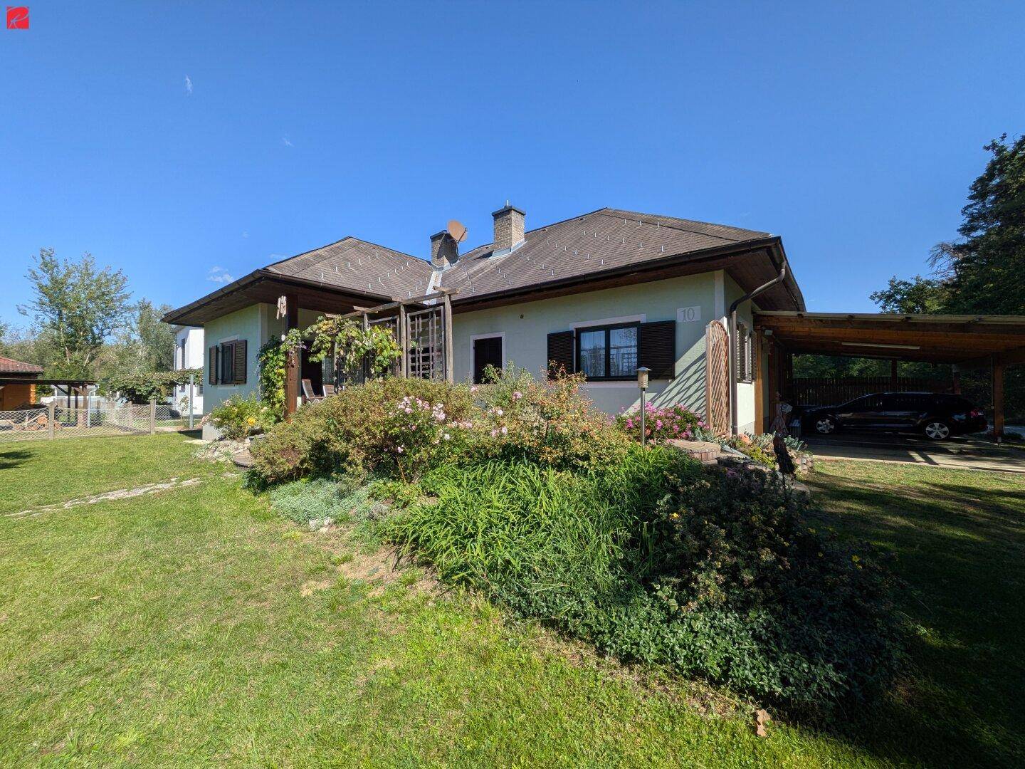 Haus mit großem Garten, überdachter Terrasse und einem Carport, umgeben von Natur.