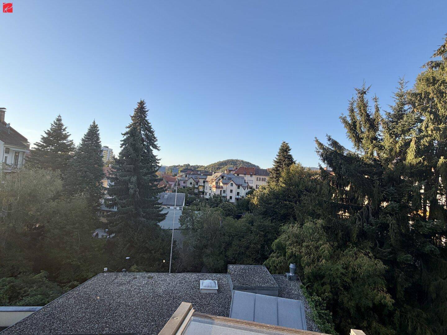 Weitblick über die Stadt und grüne Hügel von der Immobilie aus unter blauem Himmel.