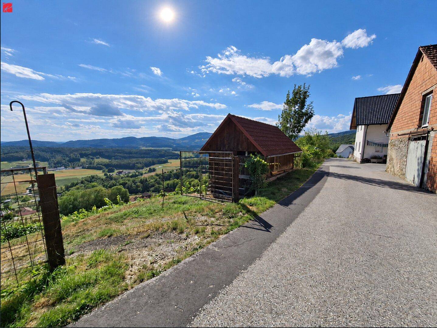 Malerischer Ausblick über ein grünes Tal und bewaldete Hügel unter strahlend blauem Himmel.
