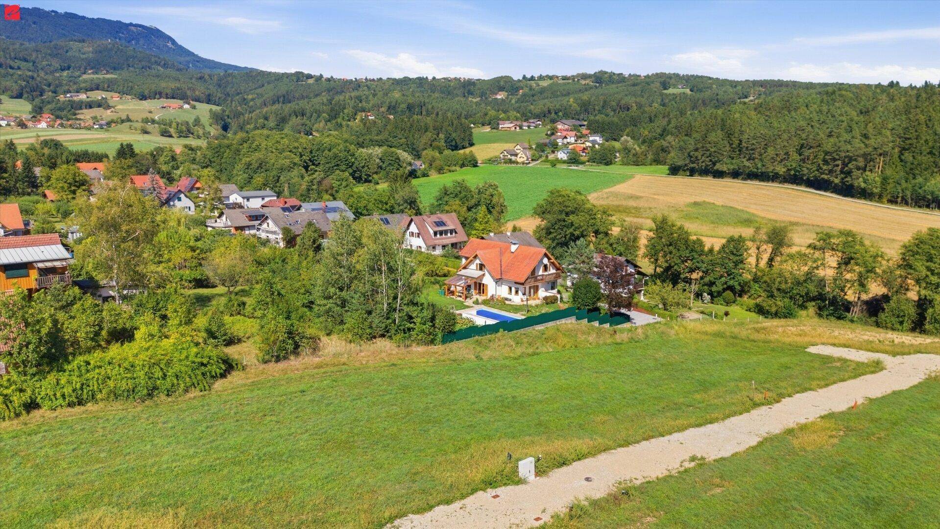 Idyllische Wohnsiedlung in hügeliger Landschaft mit Häusern, Gärten und einem Pool.