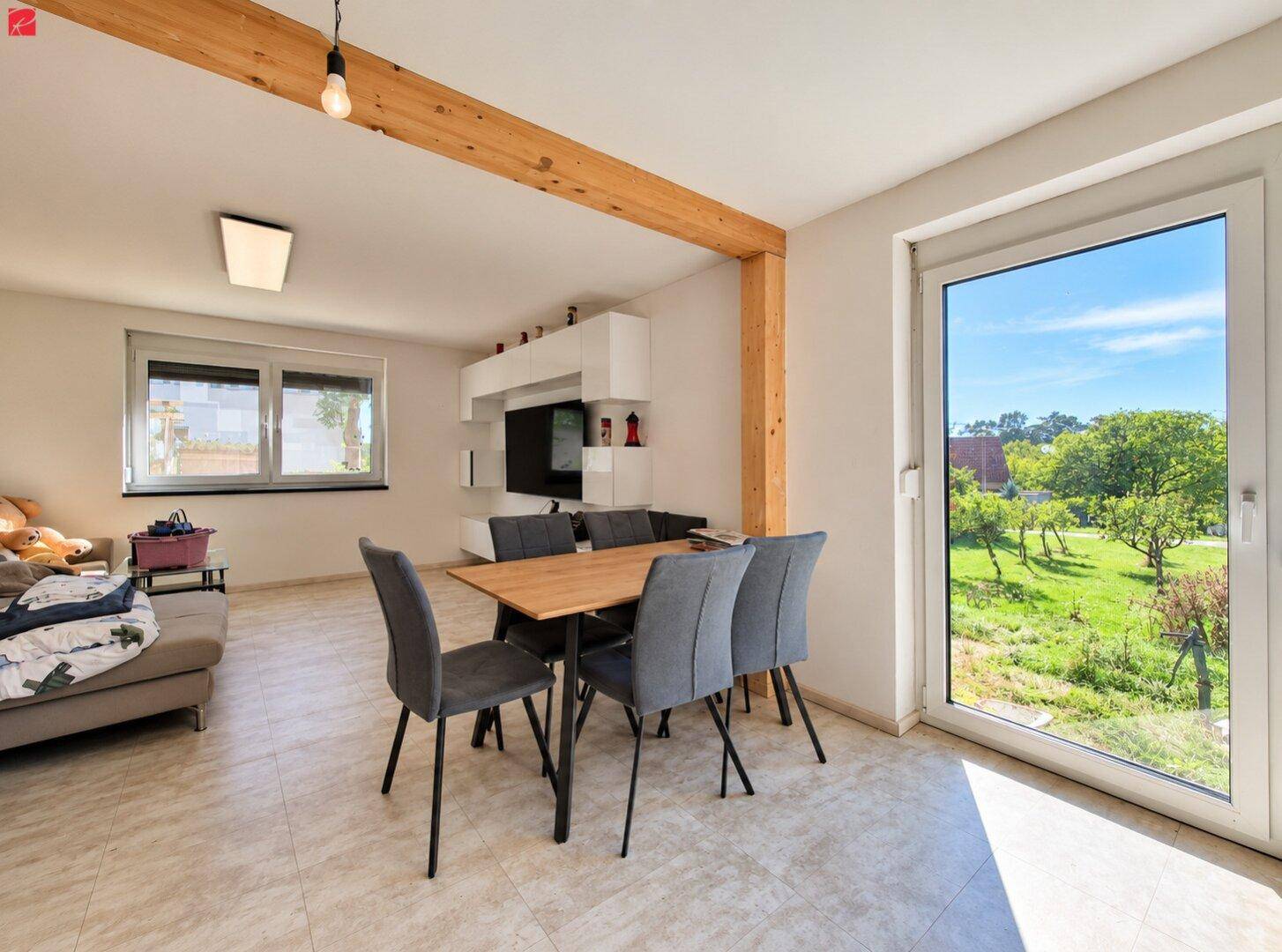 Offener Wohn-Essbereich mit Holzbalken, Esstisch und großem Fenster mit Blick in den Garten.