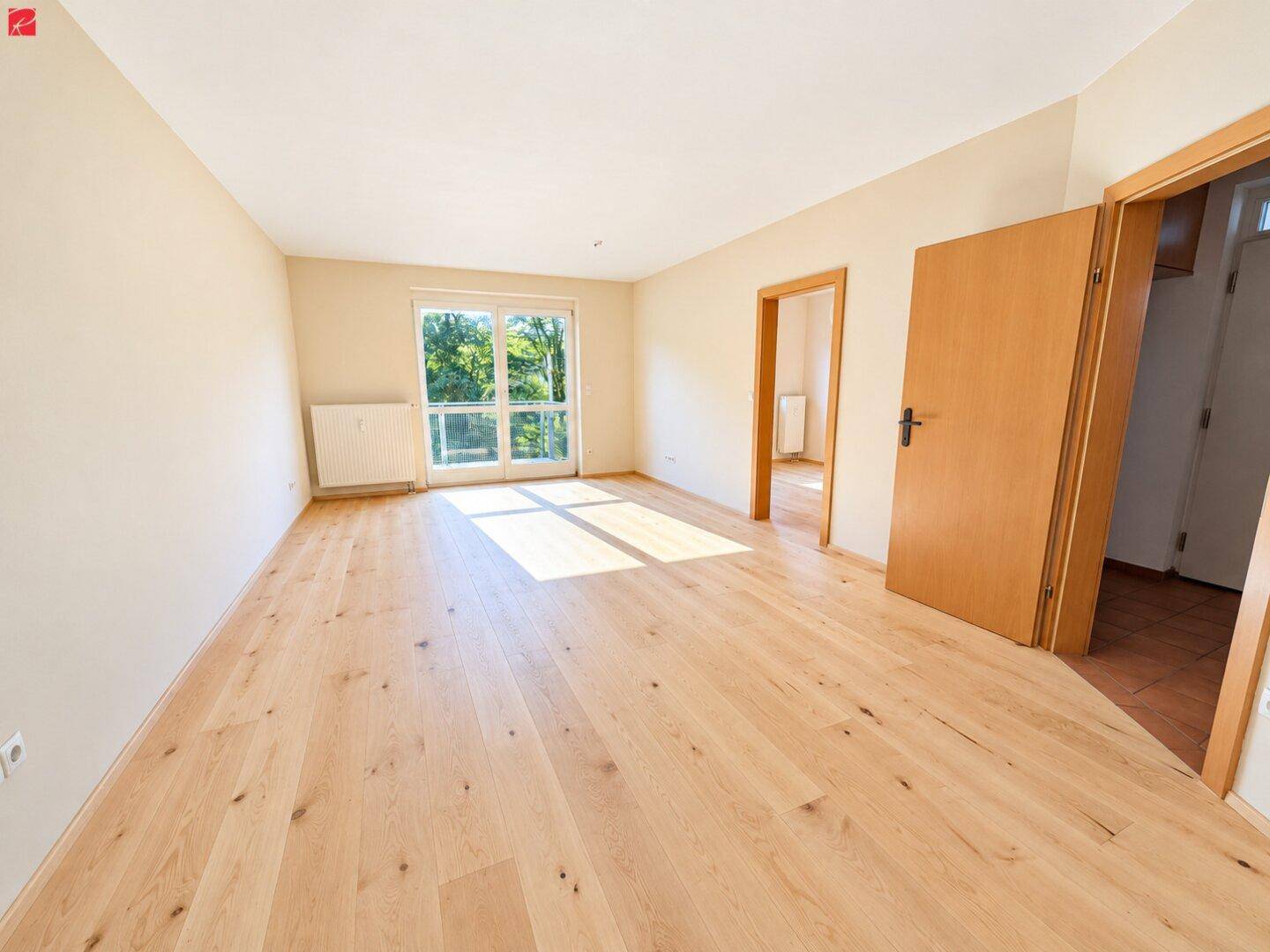 Geräumiges Wohnzimmer mit hellem Holzboden und Zugang zu einem Außenbereich, ideal für Entspannung.