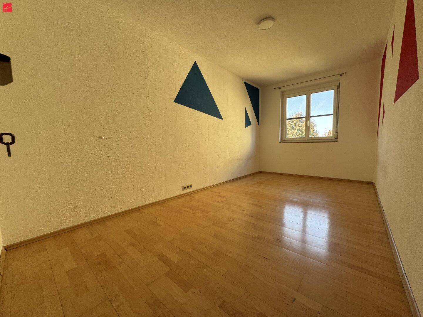 Helles Zimmer mit Parkettboden und farbenfroher Wandgestaltung, ideal als Kinder- oder Arbeitszimmer nutzbar.