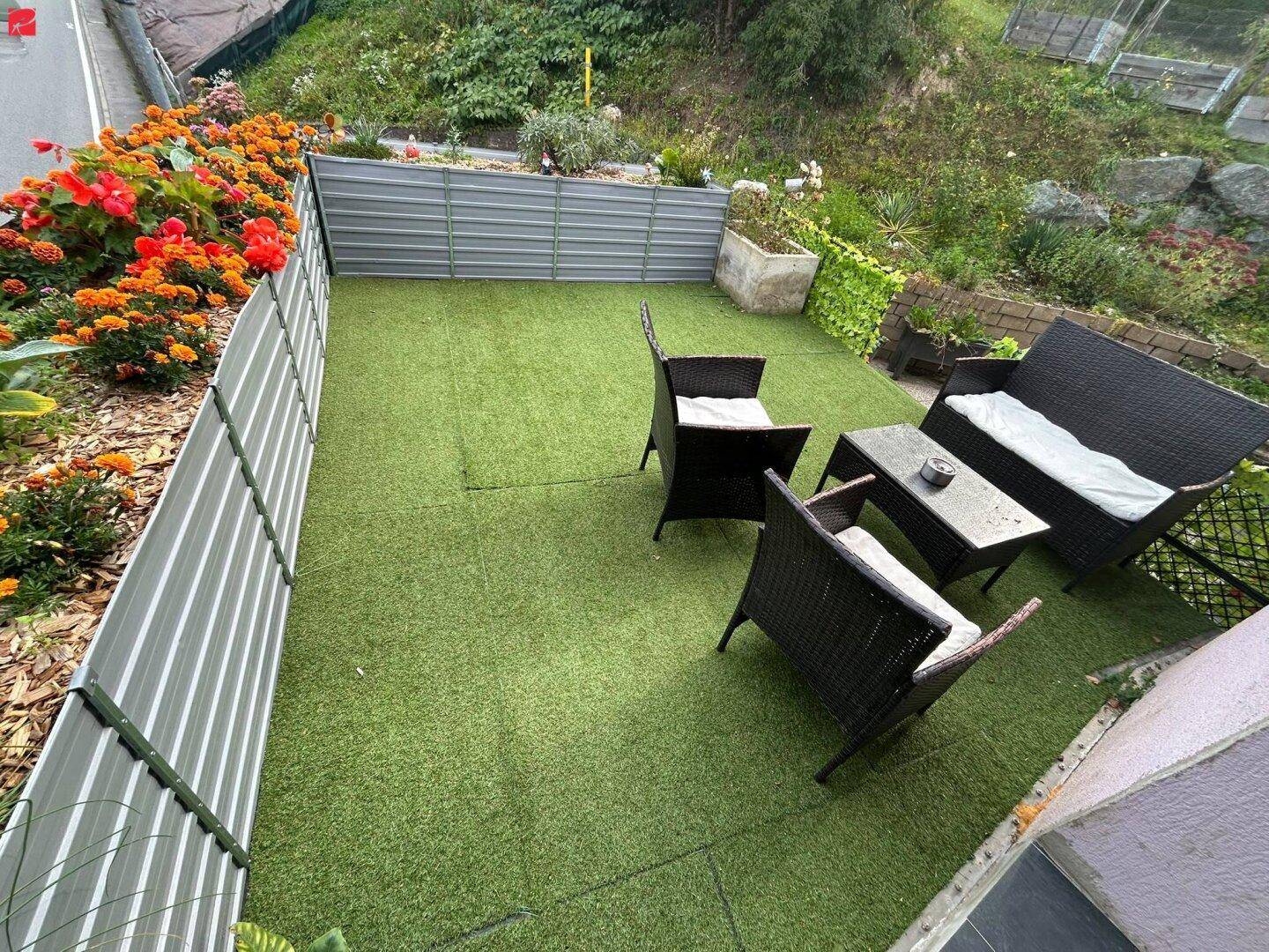 Kleine, pflegeleichte Gartenterrasse mit Kunstrasen und gemütlicher Sitzgruppe.
