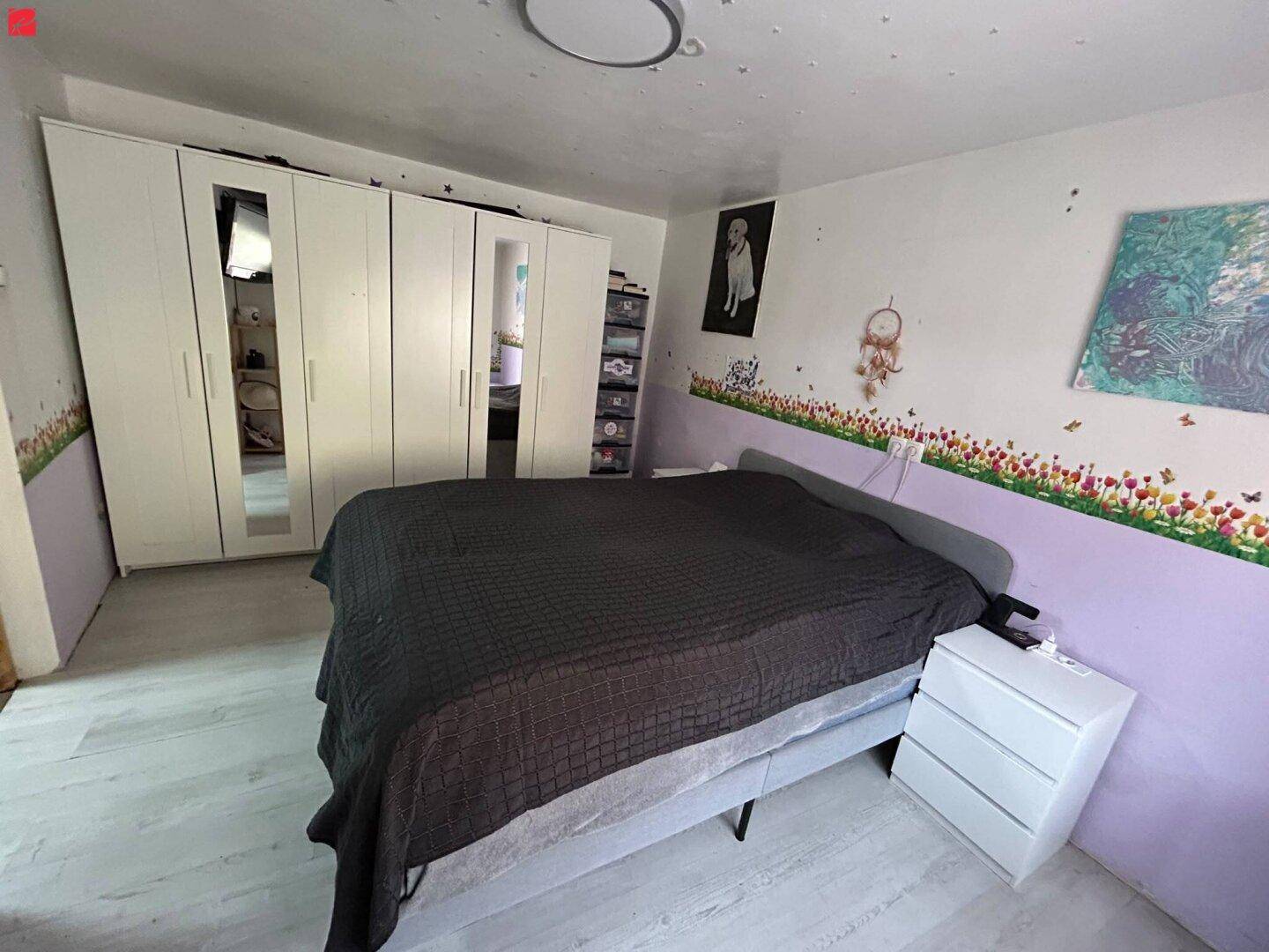 Schlafzimmer mit großem Bett, weißem Kleiderschrank und hellen Wänden.