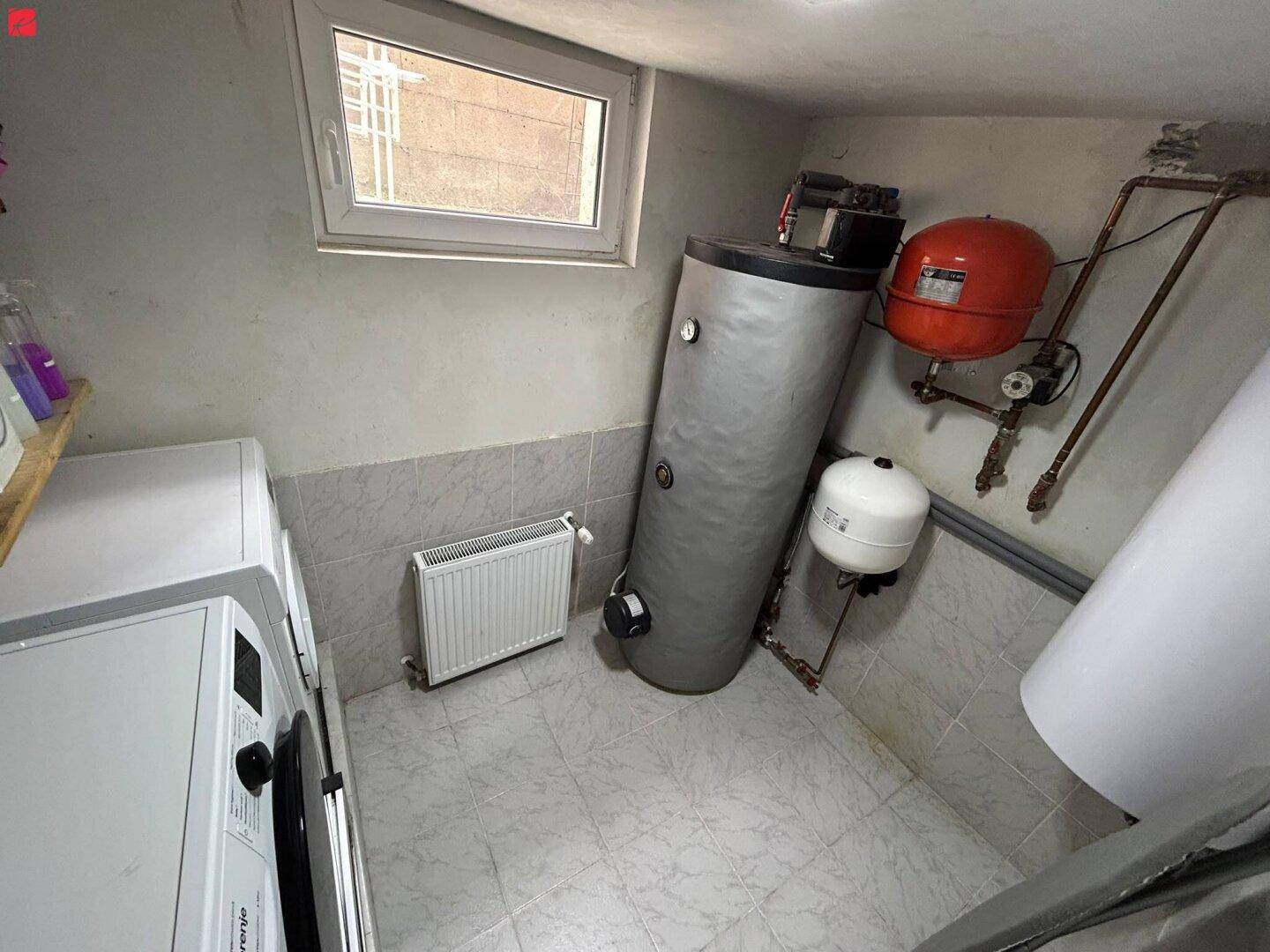 Funktionaler Hauswirtschaftsraum im Keller mit Warmwasserspeicher und Waschmaschine.