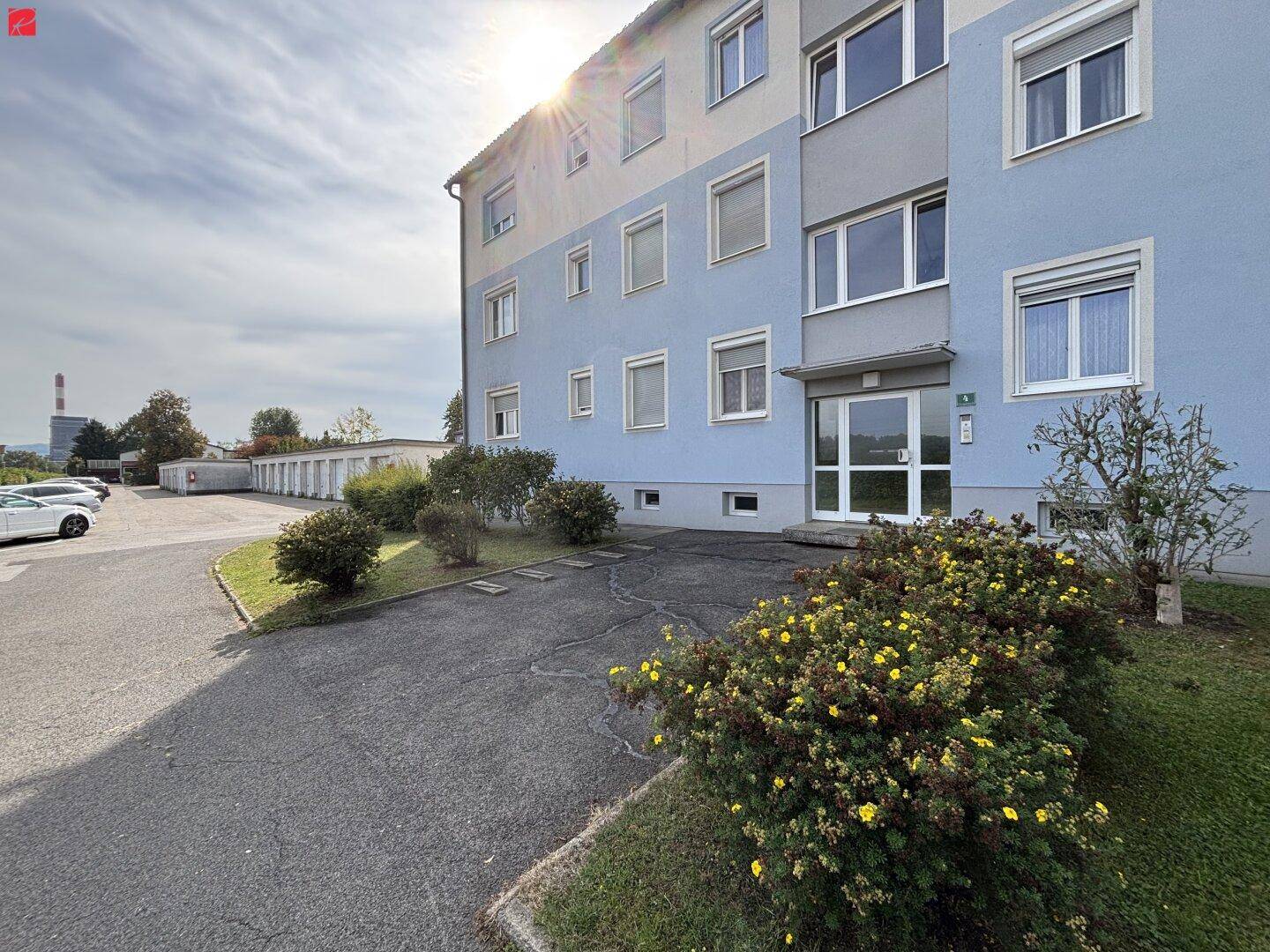 Mehrfamilienhaus mit blauer Fassade, Eingangsbereich und Parkplätzen.