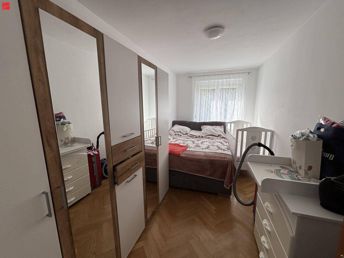 Gemütliches Schlafzimmer mit Parkettboden, Spiegelschrank und Babybett.
