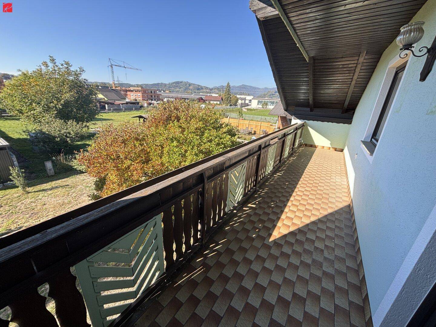 Langer Balkon mit Holzbalkongeländer und weitem Blick über die Nachbarschaft und die Berge.