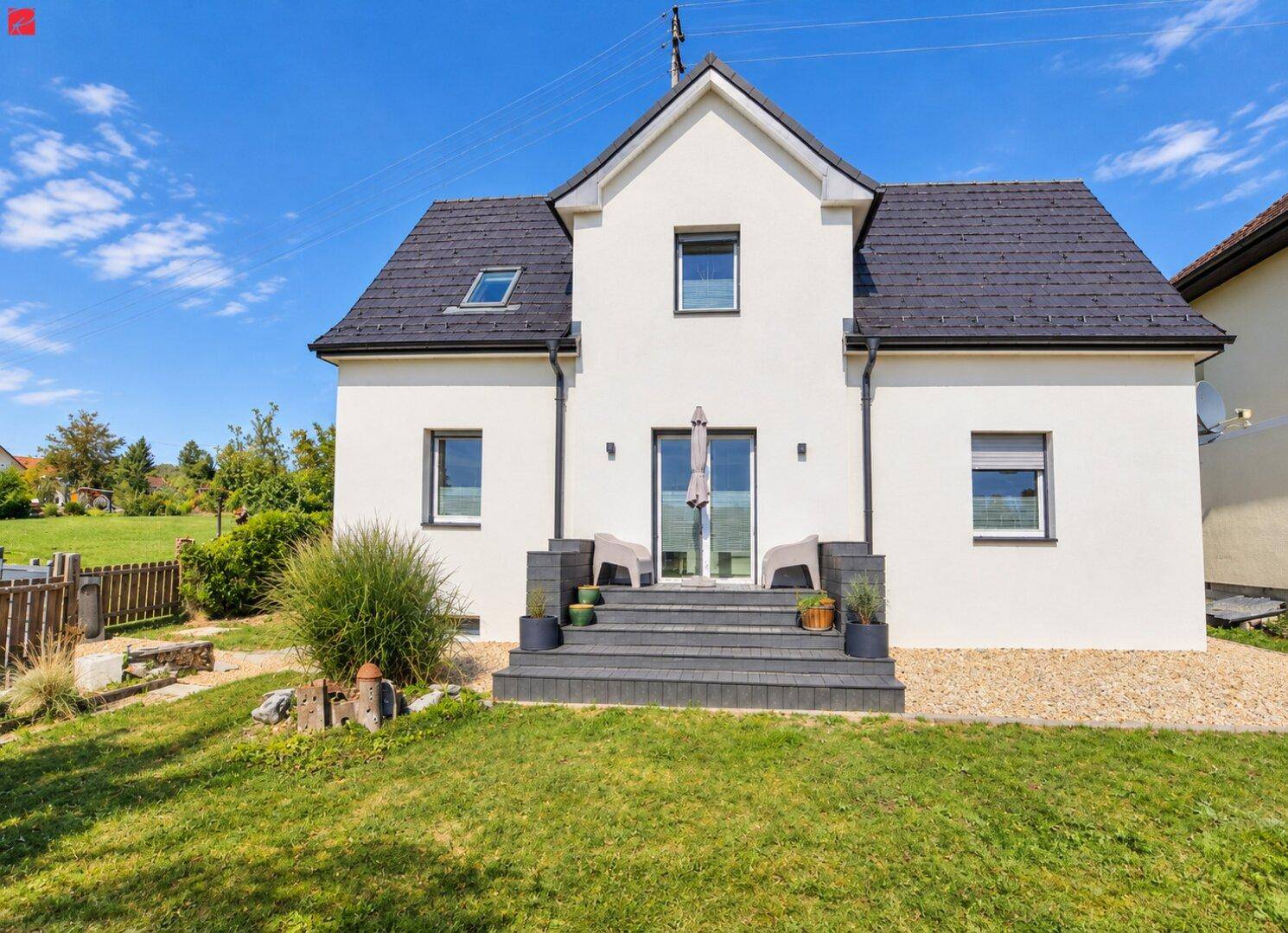 Rückansicht des Hauses mit kleiner Terrasse, Rasenfläche und Blick ins Grüne.