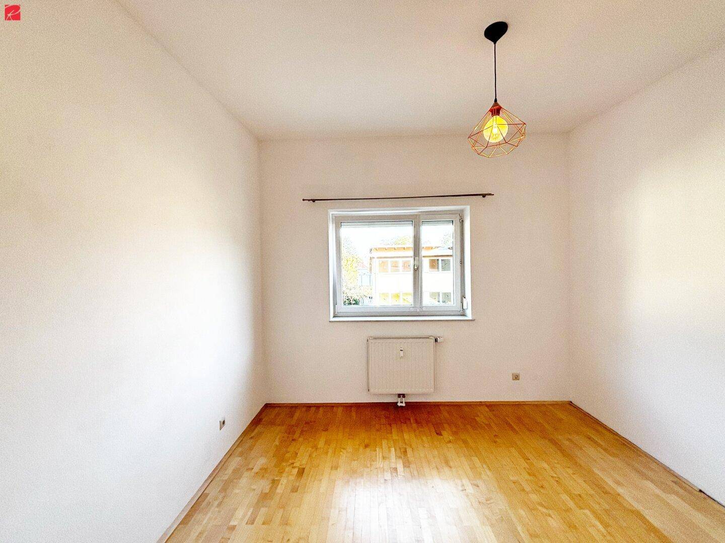 Helles Zimmer mit Holzboden, weißen Wänden und einem Fenster, das viel Tageslicht hereinlässt.