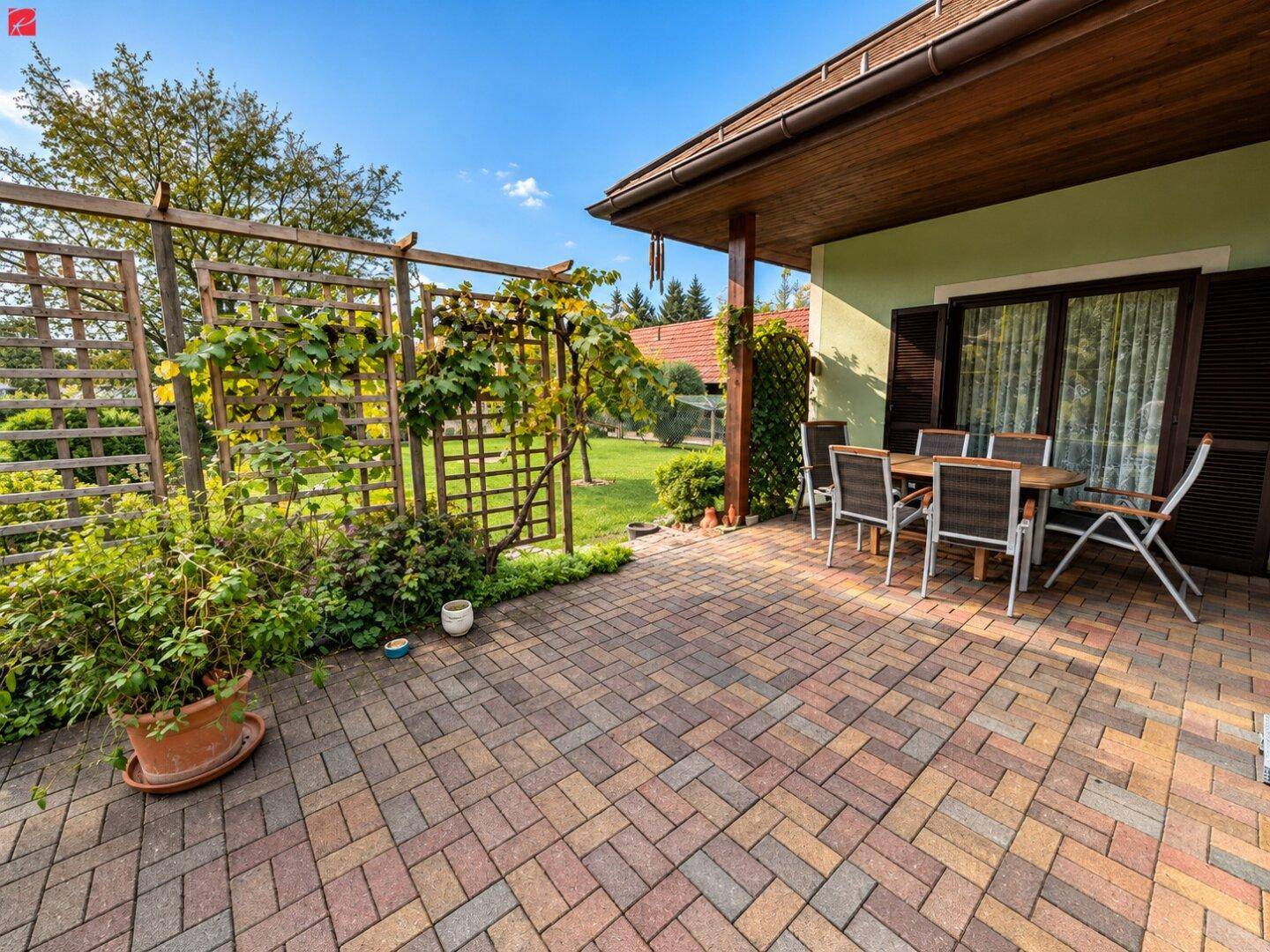Gepflasterte Terrasse mit Gartenmöbeln, Pergola und Blick ins Grüne.