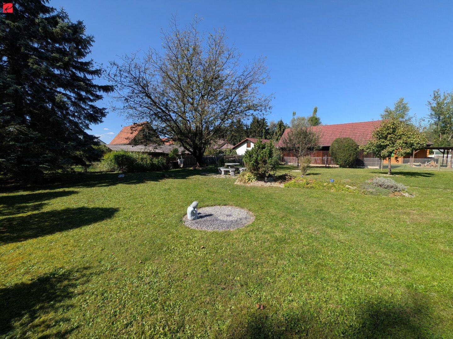 Großer, gepflegter Garten mit Rasenfläche, Bäumen und Sitzgelegenheit.