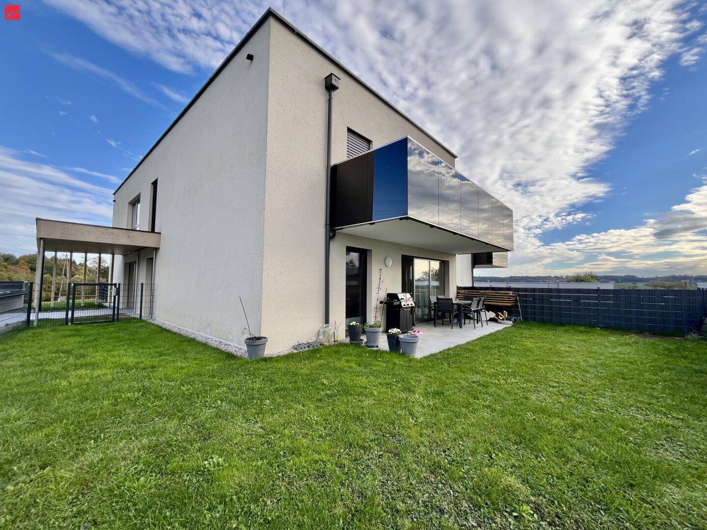 Modernes Einfamilienhaus mit Terrasse, Garten und Glasbalkon unter blauem Himmel.