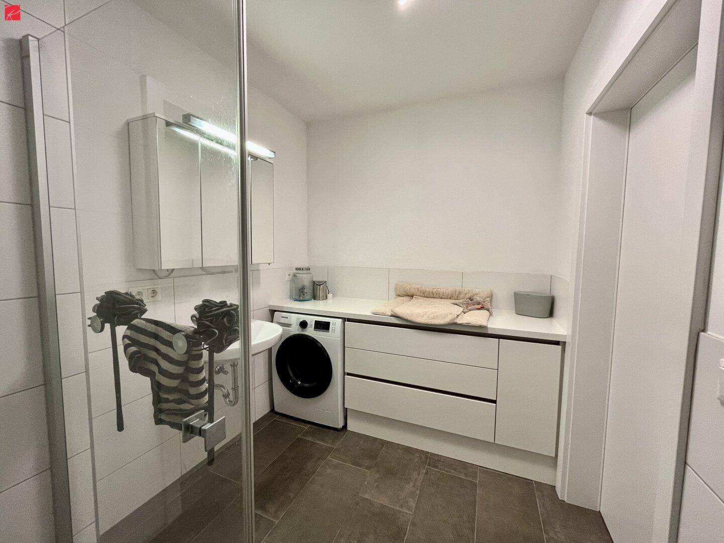 Modernes Badezimmer mit Waschbecken, Spiegelschrank und integrierter Waschmaschine.