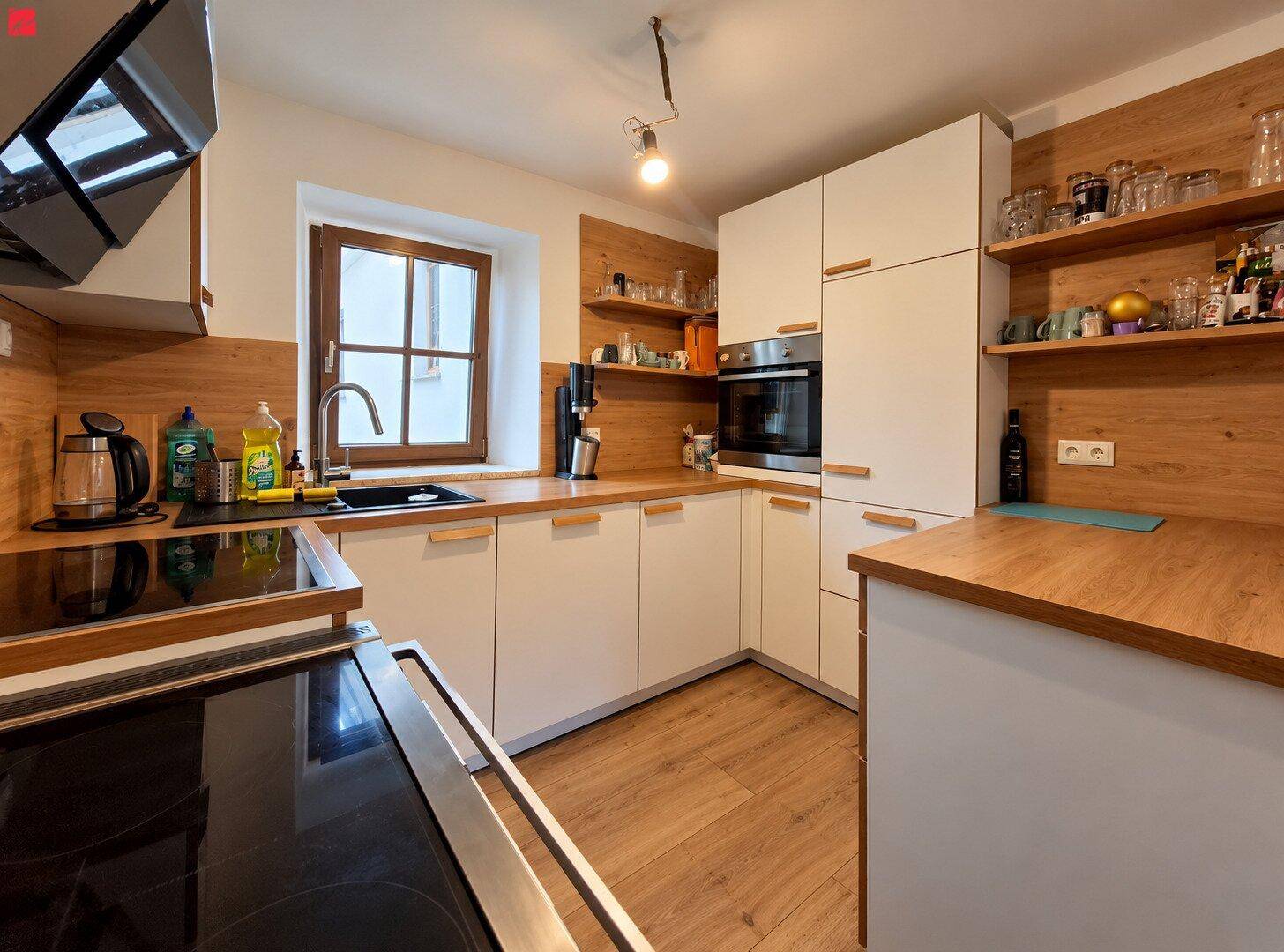 Moderne Küche mit weißen Schränken, Holz-Arbeitsplatten und integrierten Geräten, inklusive Fenster.