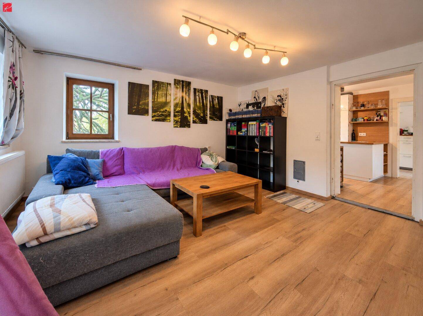 Gemütliches Wohnzimmer mit großem Ecksofa, Laminatboden und Blick in den Küchenbereich.