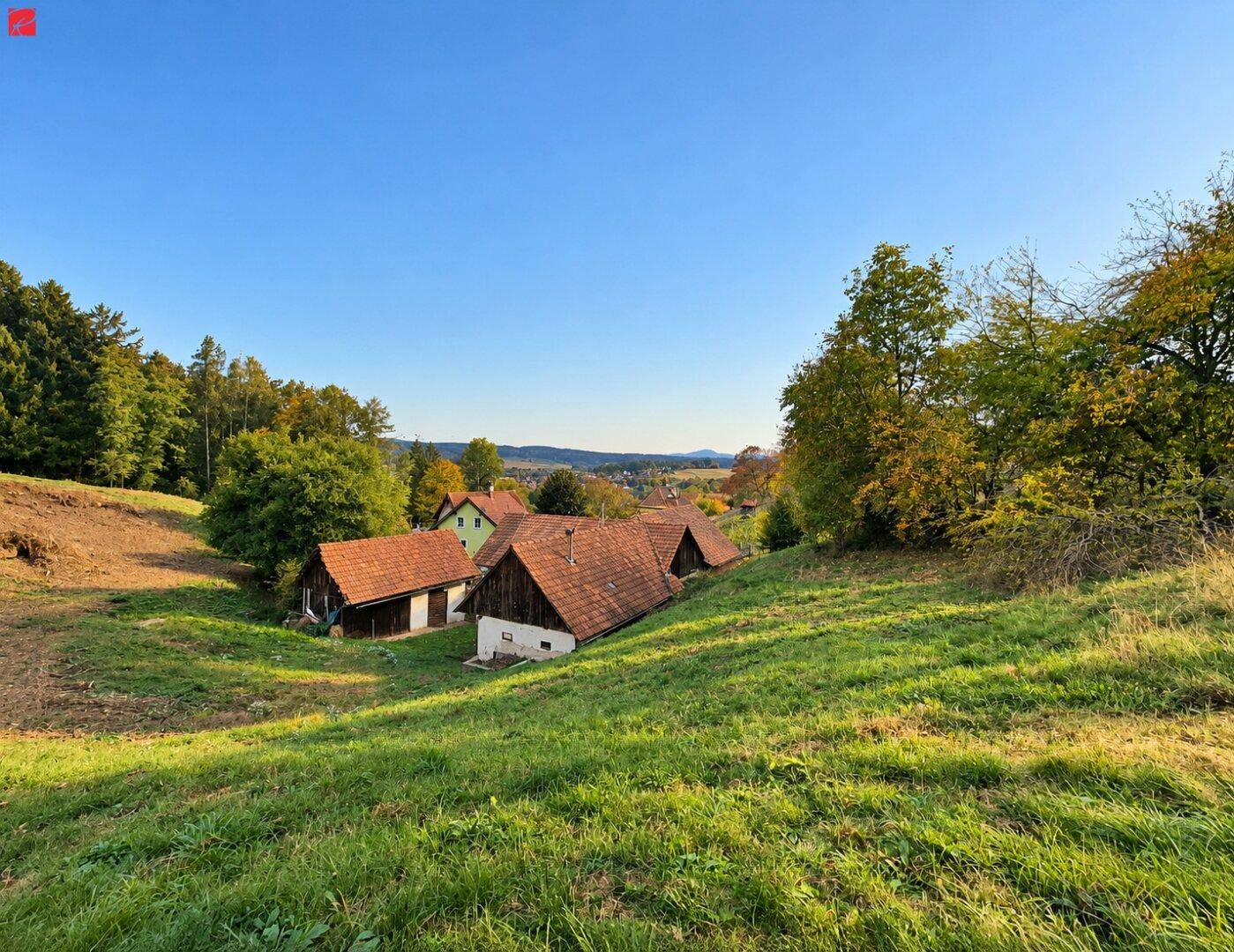 Weitläufige Landschaft mit grünen Hügeln und traditionellen Häusern unter blauem Himmel.