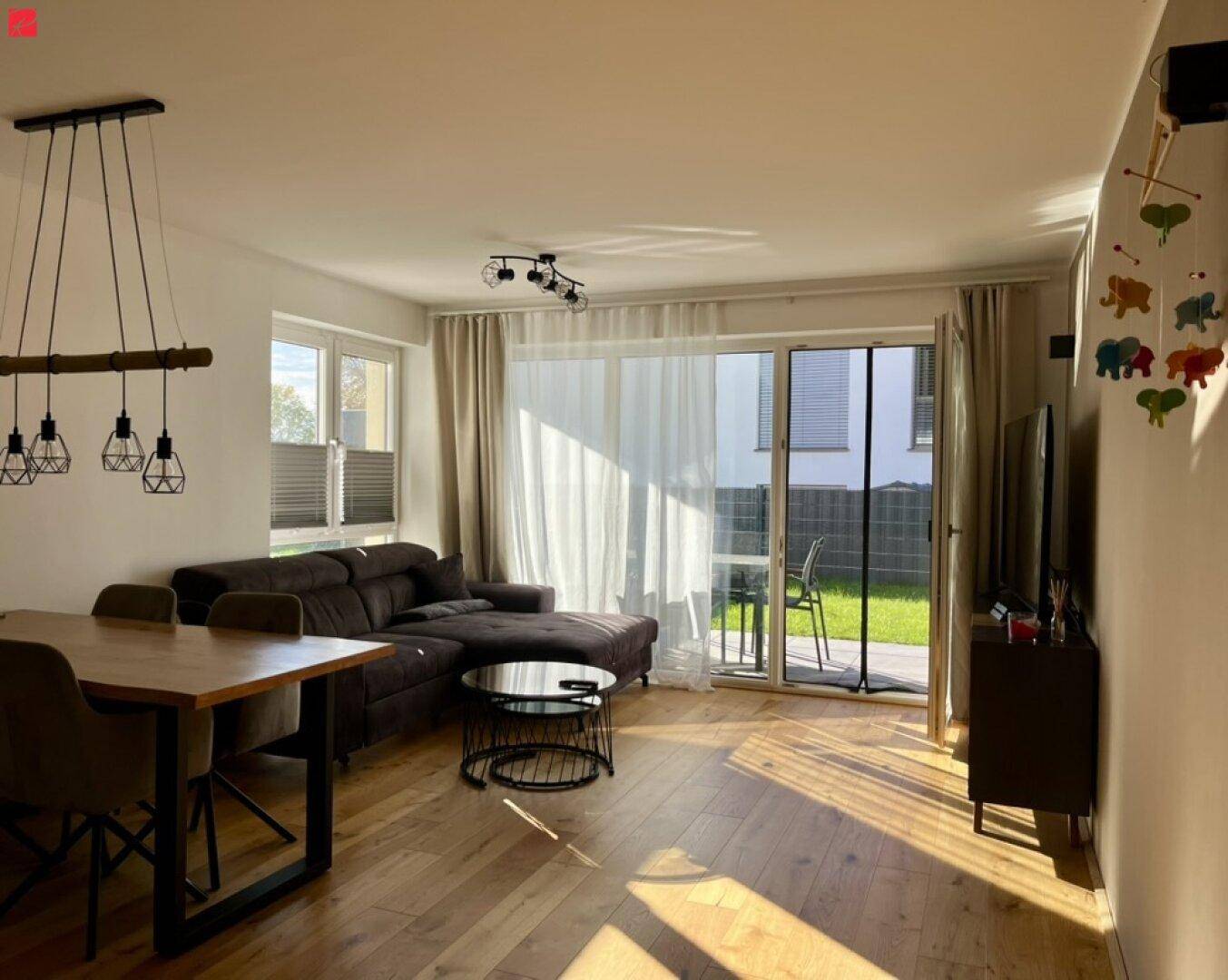 Helles Wohnzimmer mit großem Sofa, Holzboden und Zugang zum Garten.