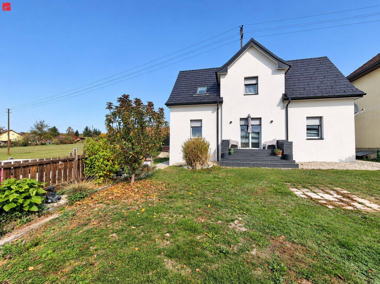 Modernes Einfamilienhaus mit weißer Fassade, dunklem Dach und gepflegtem Gartenbereich.