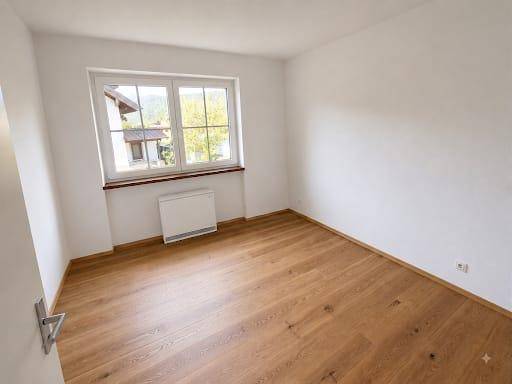 Leeres Zimmer mit hellem Holzfußboden, weißen Wänden und einem großen Fenster.