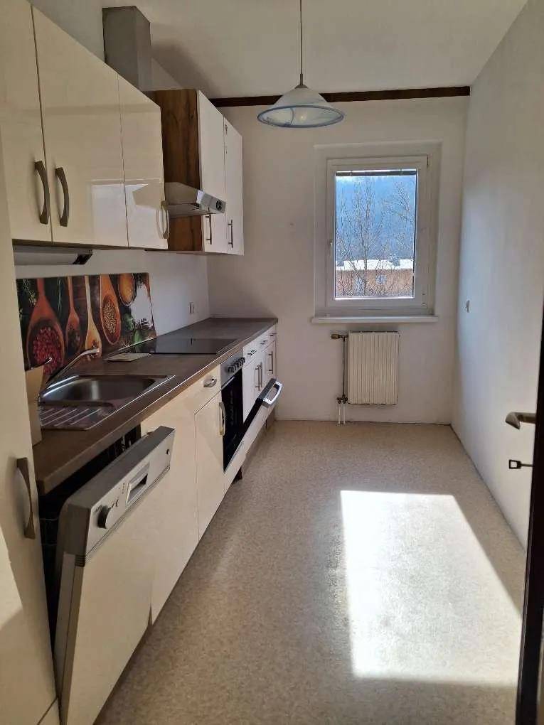 Funktionale Küche mit weißen Schränken, Spülmaschine und einem Fenster, das Tageslicht hereinlässt.