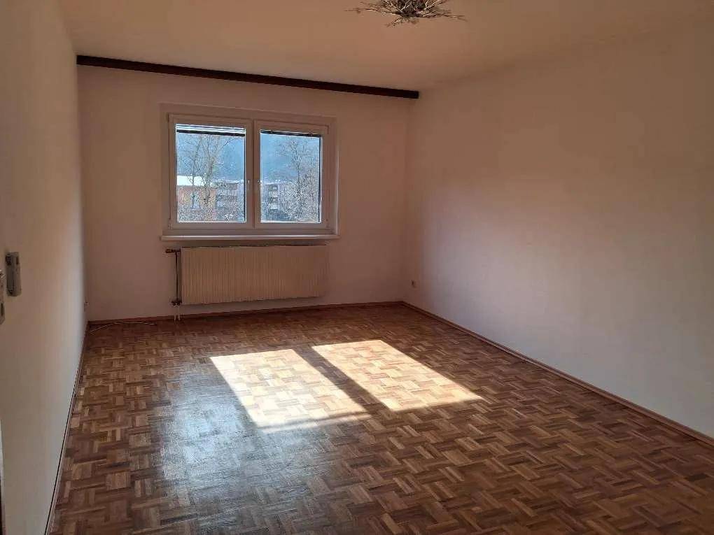 Helles Schlafzimmer mit Fischgrätparkett und großem Fenster, das viel Sonnenlicht hereinlässt.