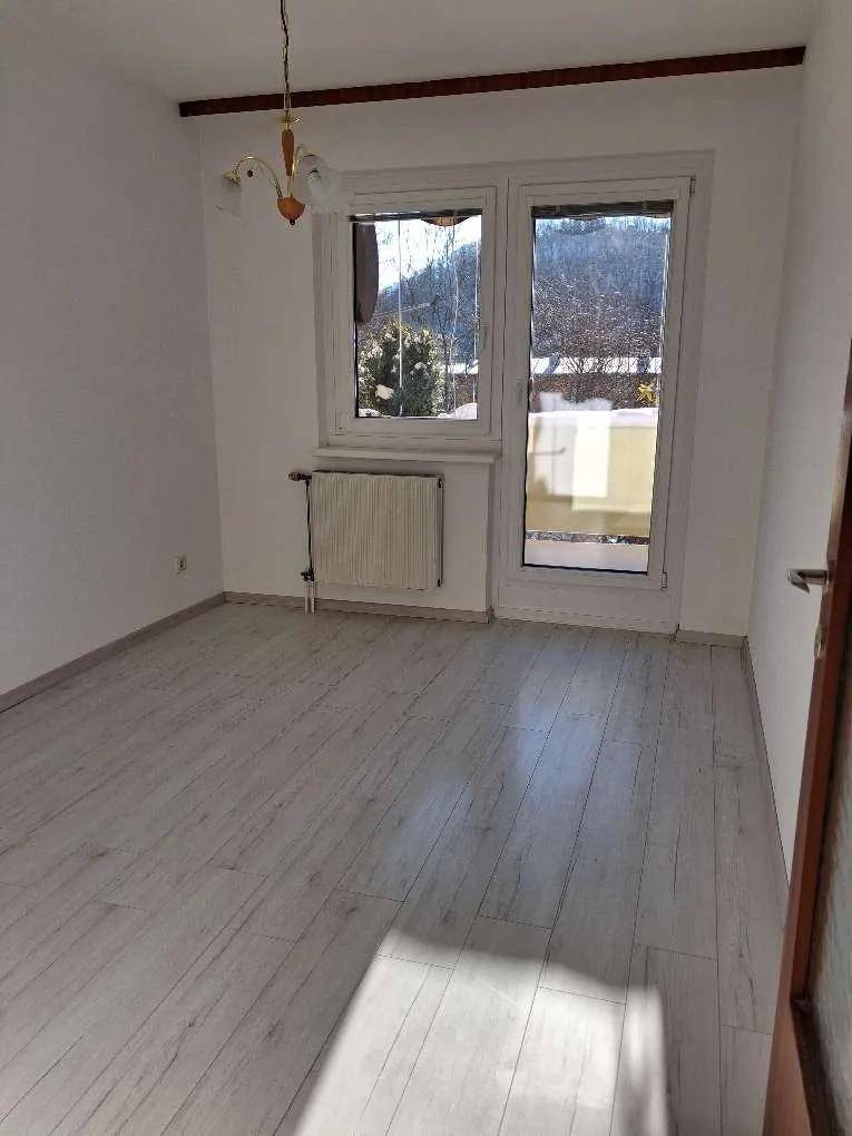 Renoviertes Zimmer mit hellem Laminatboden und Zugang zu einem Balkon, bietet einen Blick ins Grüne.