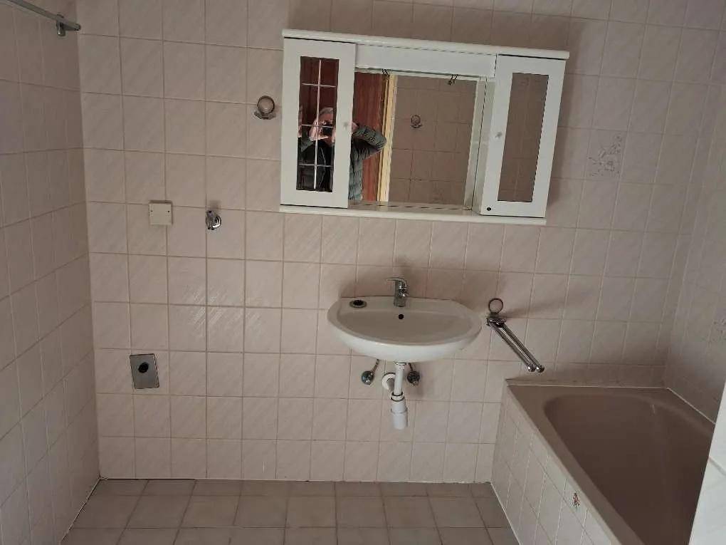 Badezimmer mit hellrosa Fliesen, einem einzelnen Waschbecken und einer Badewanne im Stil der 80er Jahre.