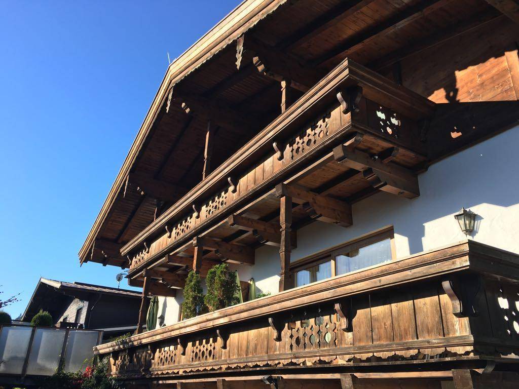 Traditionelles Alpenhaus mit kunstvoll geschnitzten Holzbalkonen und weißer Fassade unter blauem Himmel.