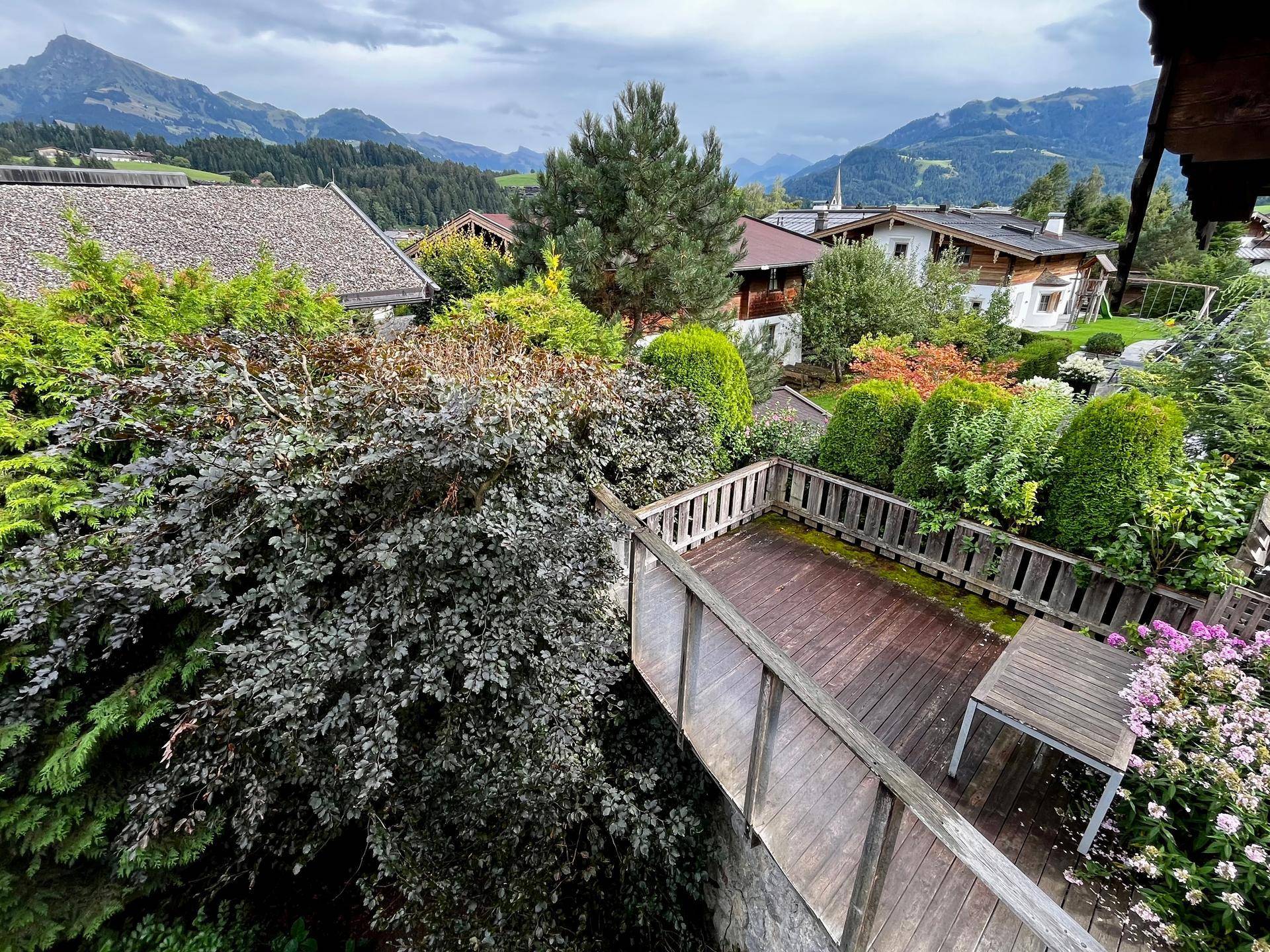 Erhöhte Holzterrasse mit Esstisch, umgeben von üppigem Grün und Panoramablick auf Häuser und Berge.