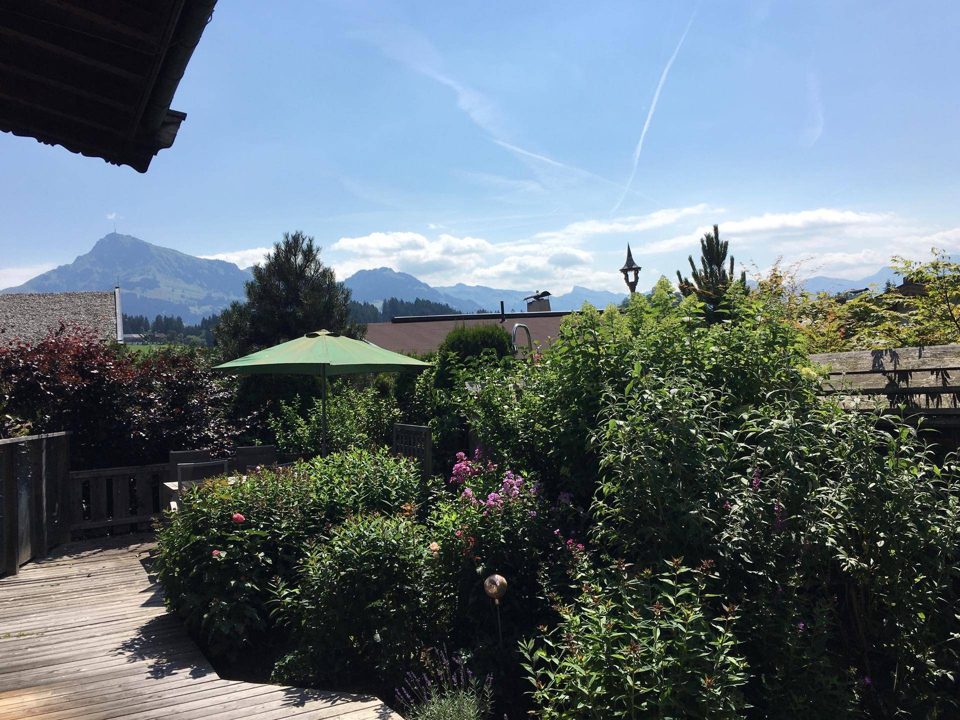 Weitläufiger Blick von der Holzterrasse auf die umliegende Berglandschaft und grüne Gärten.