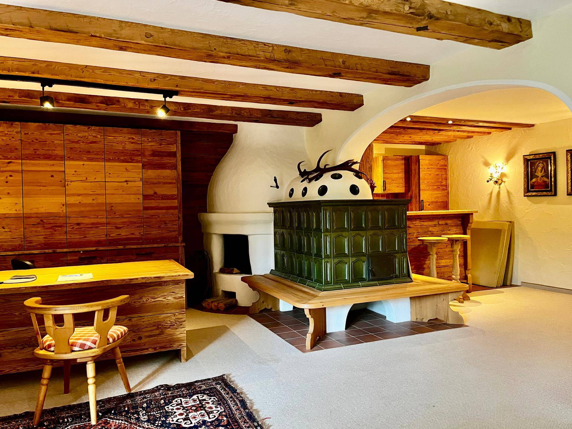 Gemütlicher Wohnbereich mit traditionellem grünen Kachelofen, Holzbalkendecke und rustikalen Holzmöbeln.