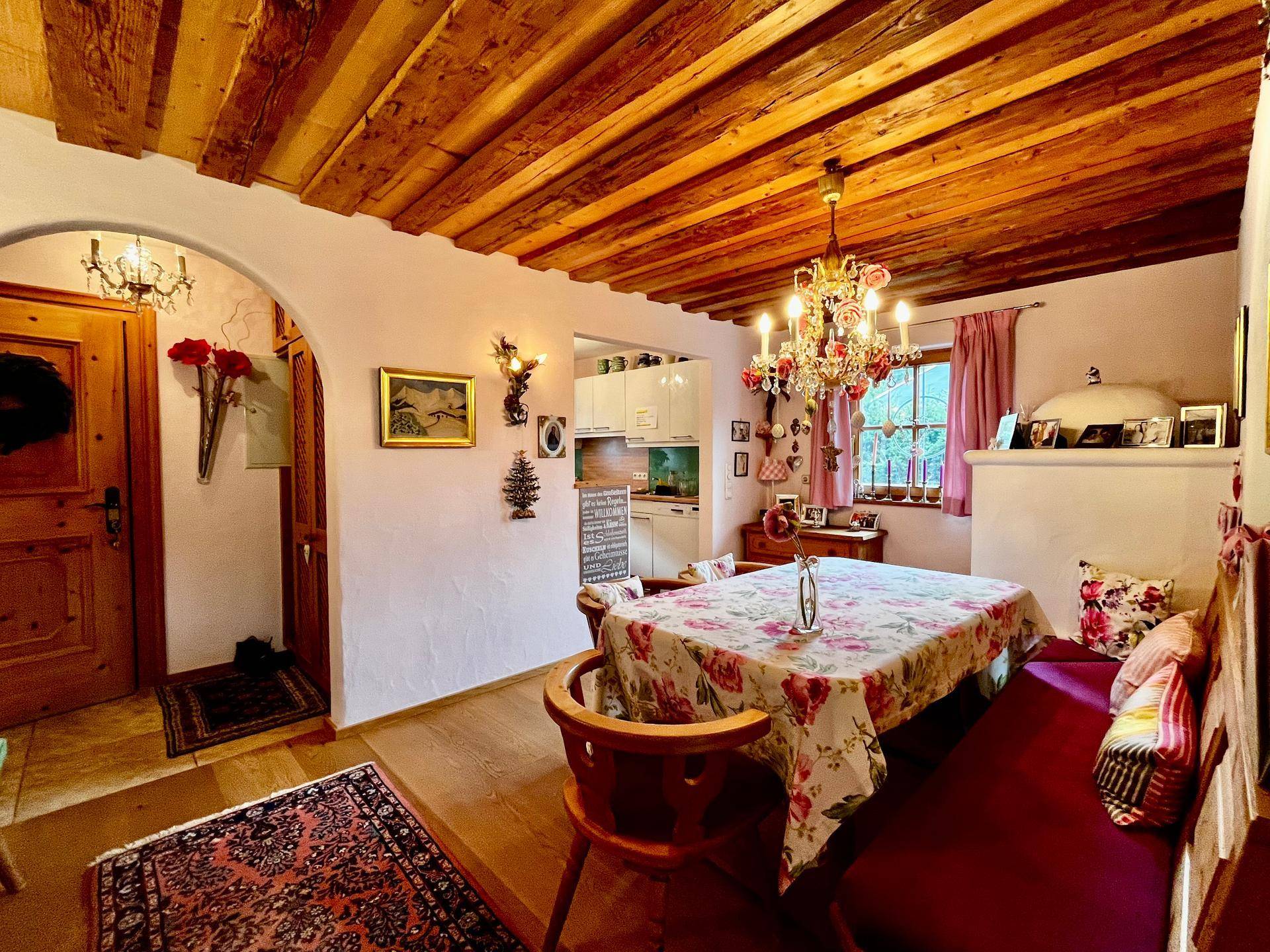 Rustikaler Essbereich mit Holzbalkendecke, traditioneller Sitzbank und Blick auf eine kleine Küche.