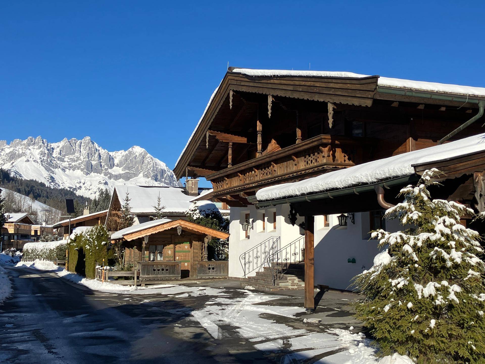 Winterlandschaft mit traditionellen Alpenhäusern, schneebedeckten Dächern und majestätischen Bergen im Hintergrund.