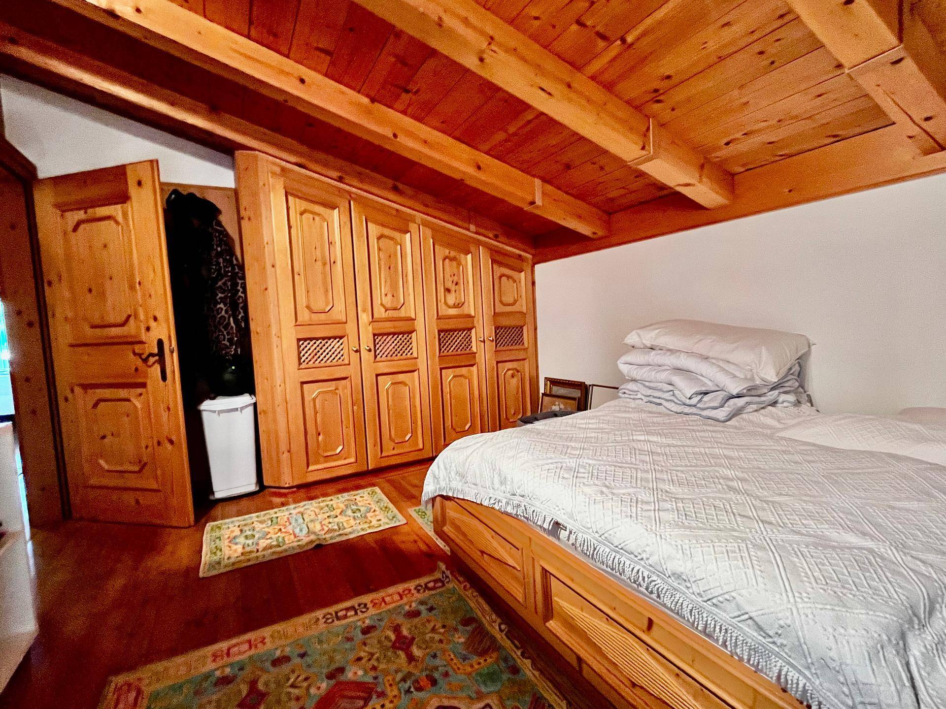 Schlafzimmer mit Holzbett, maßgefertigten Holzschränken, Holzbalkendecke und traditionellen Teppichen.