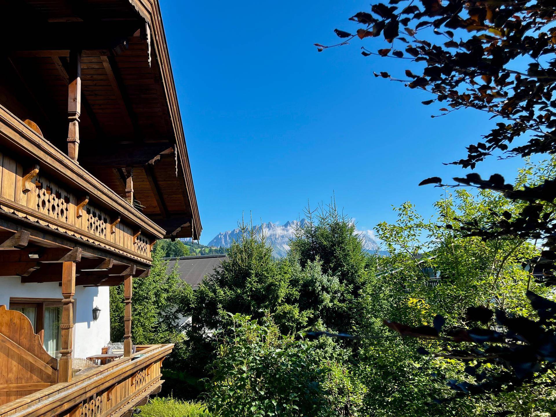 Balkonblick auf grüne Bäume und die beeindruckende Bergkulisse unter einem strahlend blauen Himmel.