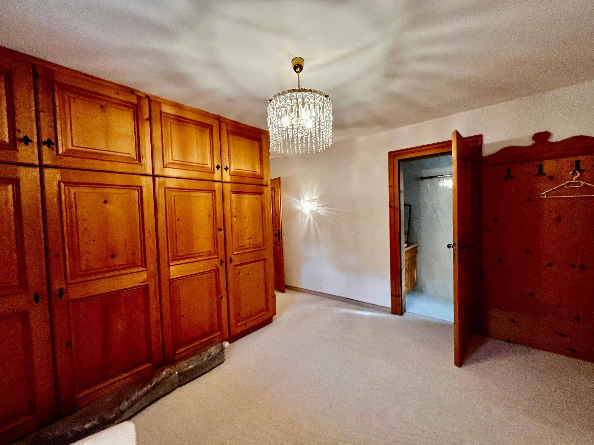 Schlafzimmer mit großen, maßgefertigten Holzschränken und einem eleganten Kronleuchter an der Decke.