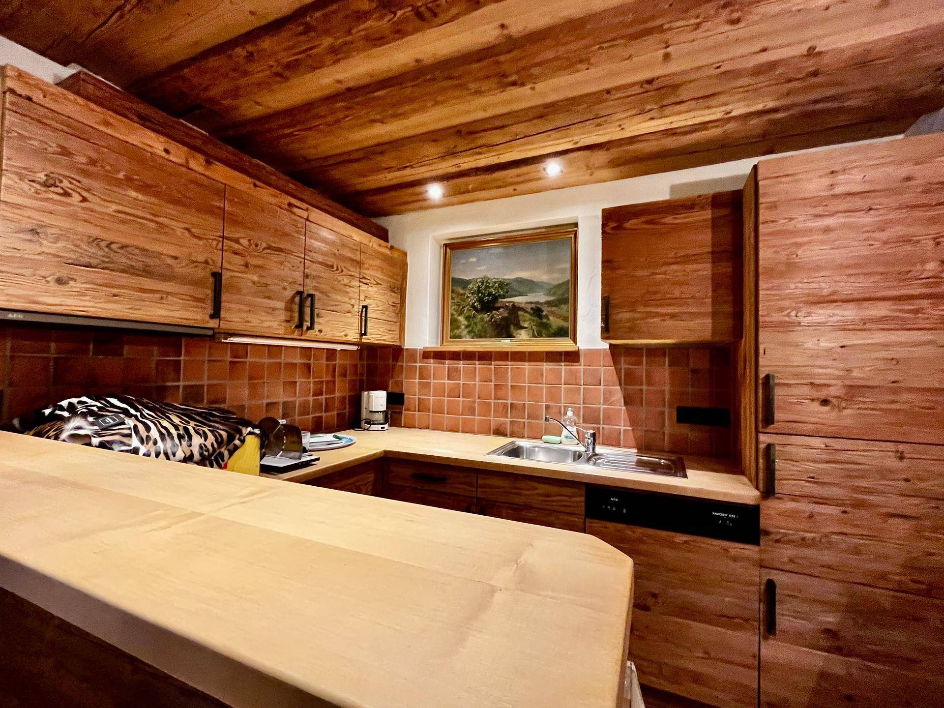 Rustikale Küche mit Holzschränken, gefliestem Spritzschutz und einem kleinen Fenster mit Landschaftsblick.