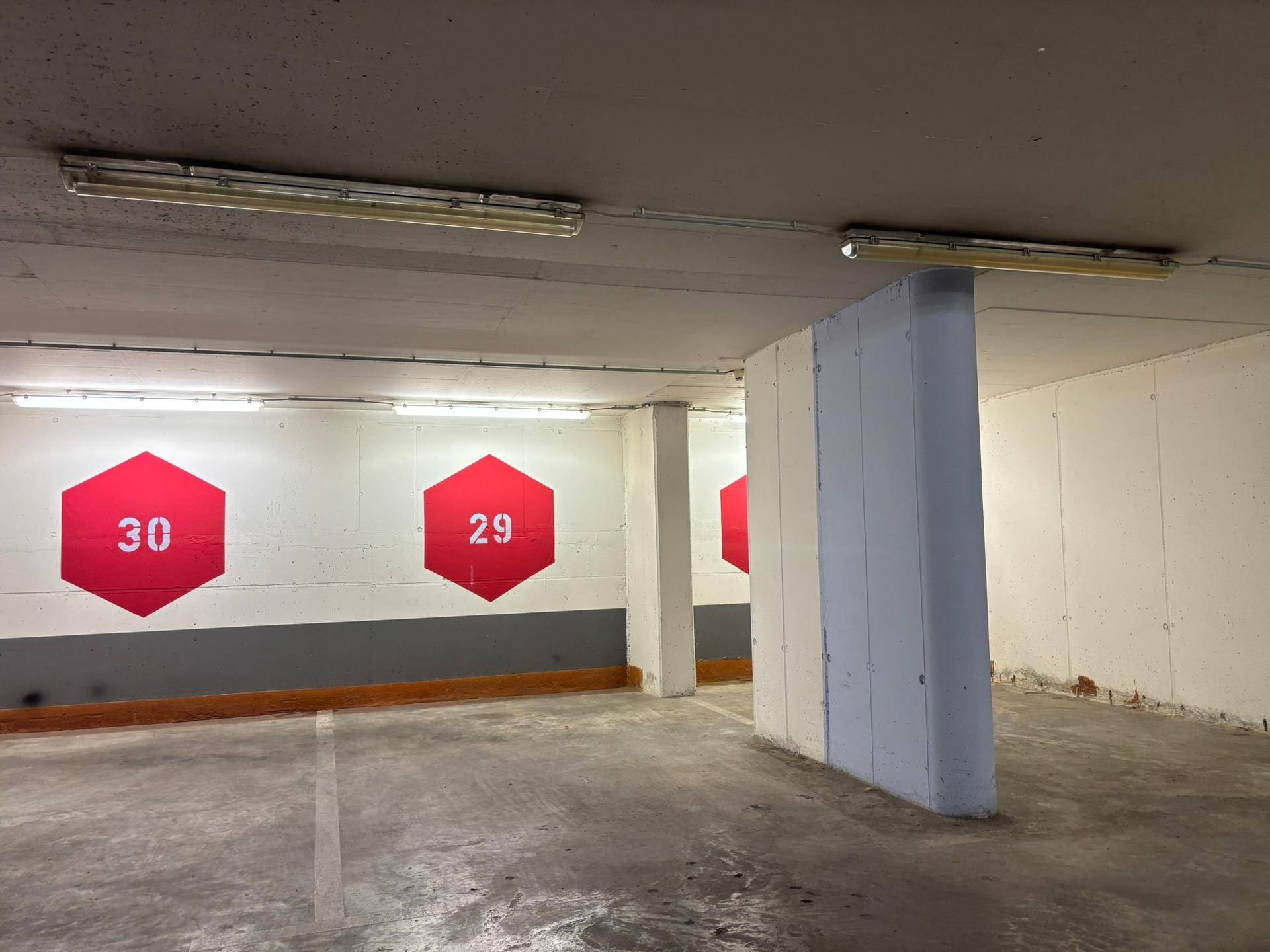 Tiefgarage mit Betonboden und Wänden, gekennzeichneten Parkplätzen und Leuchtstoffröhren.