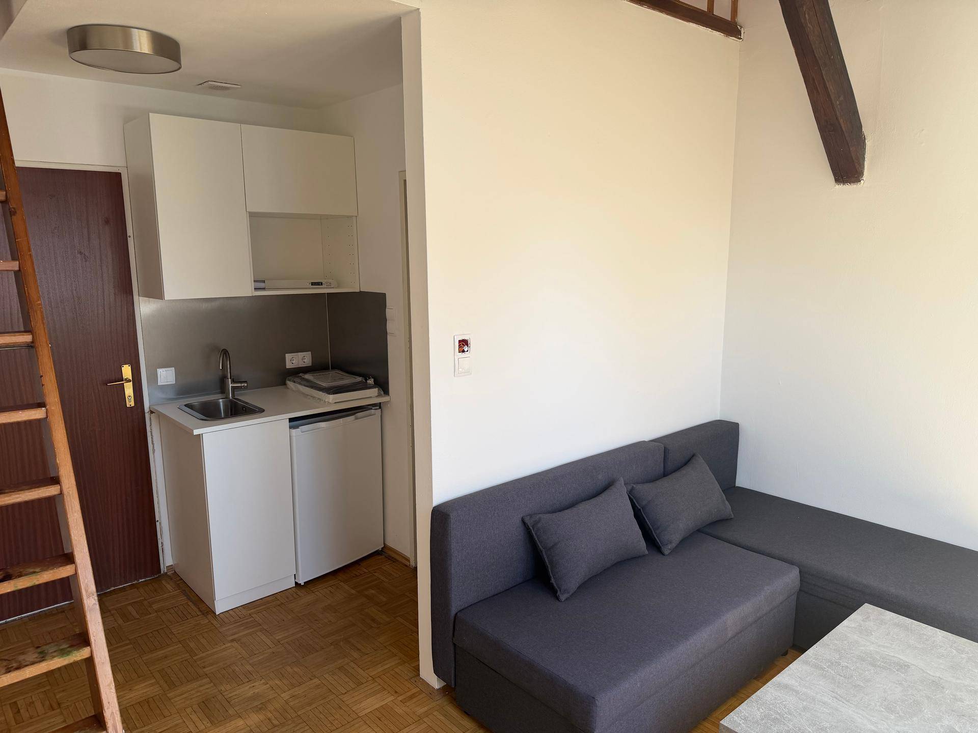 Wohnbereich mit grauem Sofa und integrierter Küchenzeile mit weißen Schränken und Spüle.