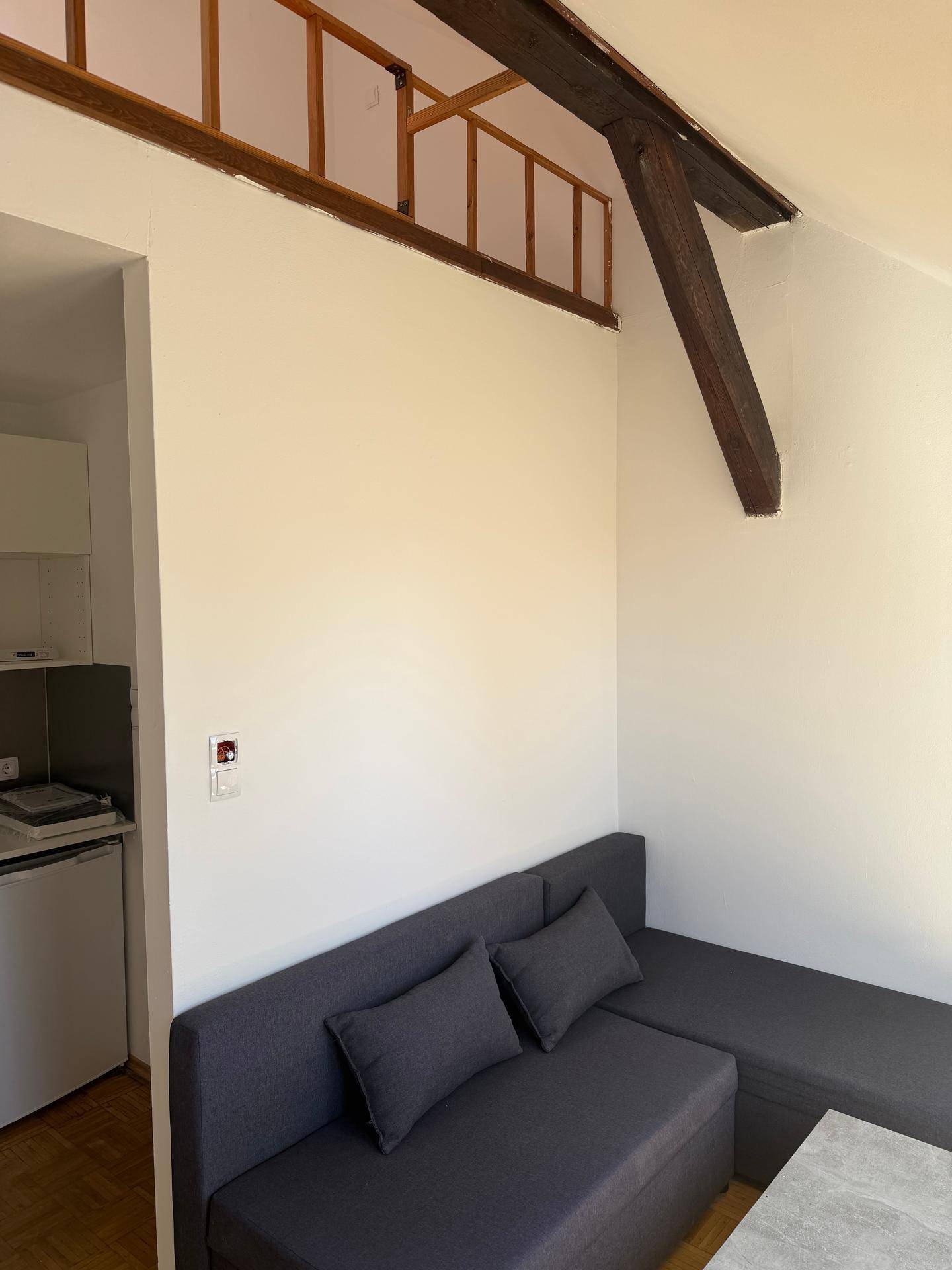 Heller Wohnbereich mit modernem grauem Sofa und sichtbaren Holzbalken, die eine Empore andeuten.