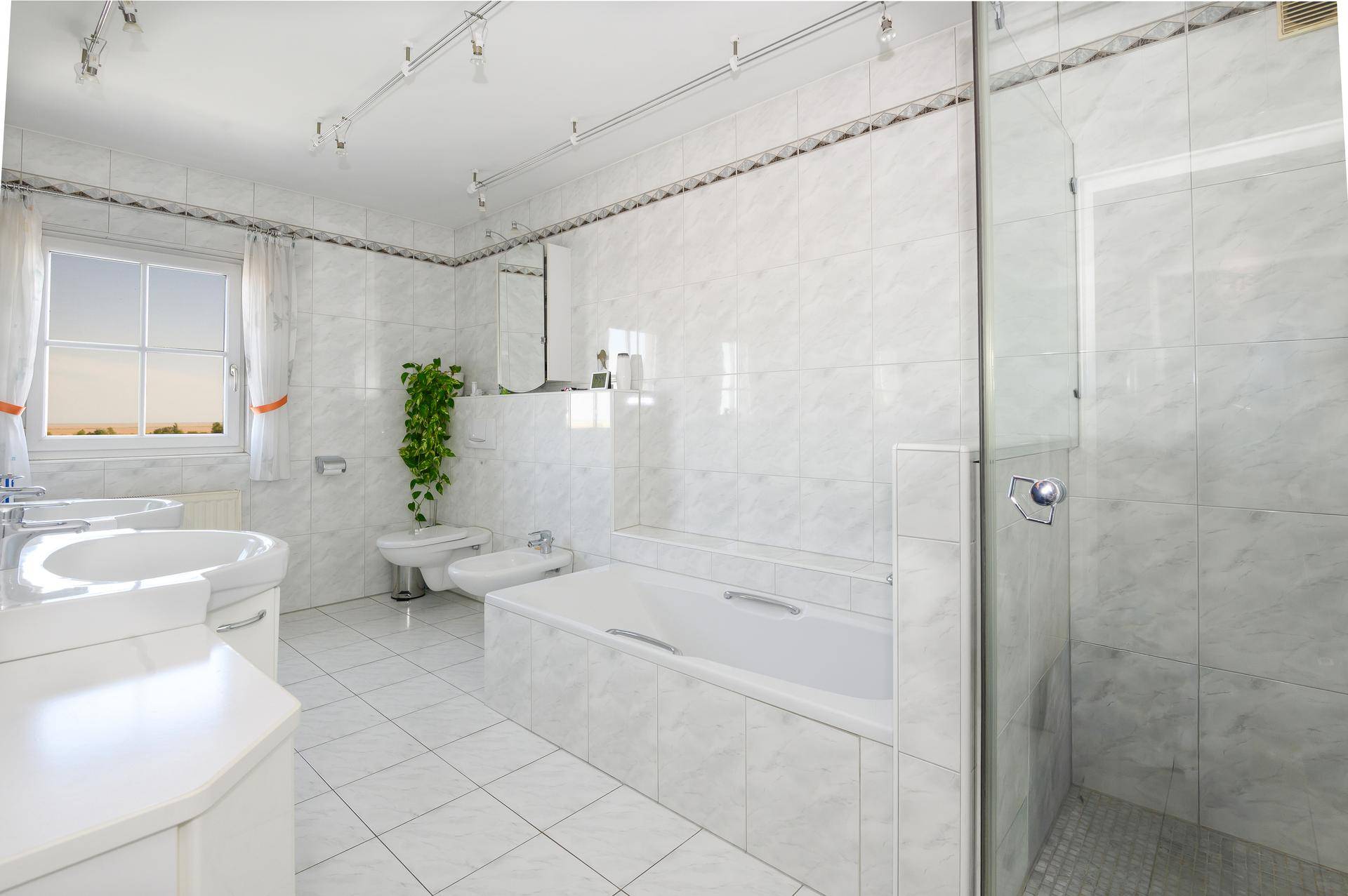 Modernes Badezimmer mit weißen Fliesen, Badewanne, Duschkabine, Bidet und Fenster für natürliche Belüftung.