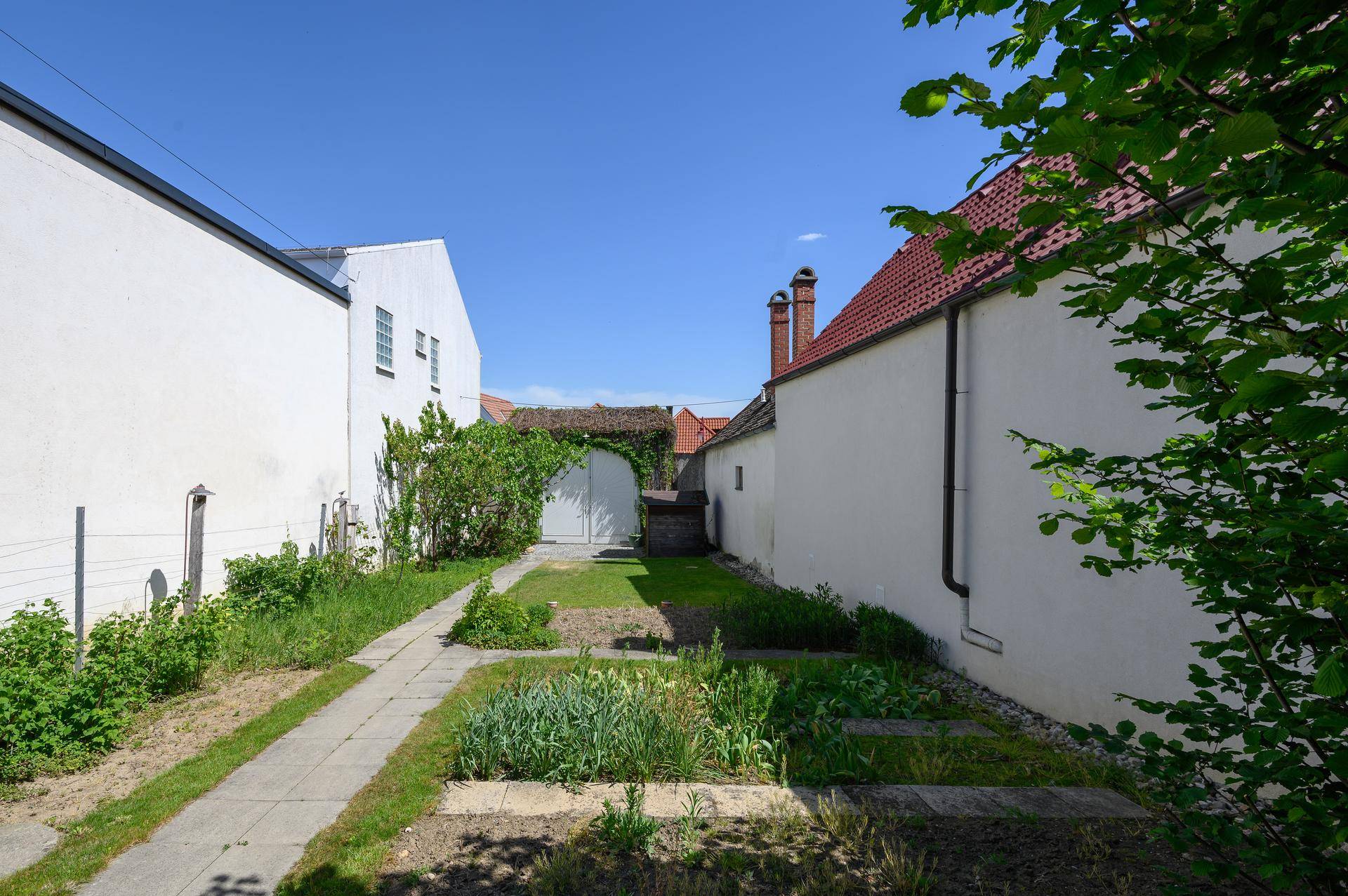 Langer Gartenweg zwischen zwei Gebäuden mit Rasenflächen und einfacher Bepflanzung.